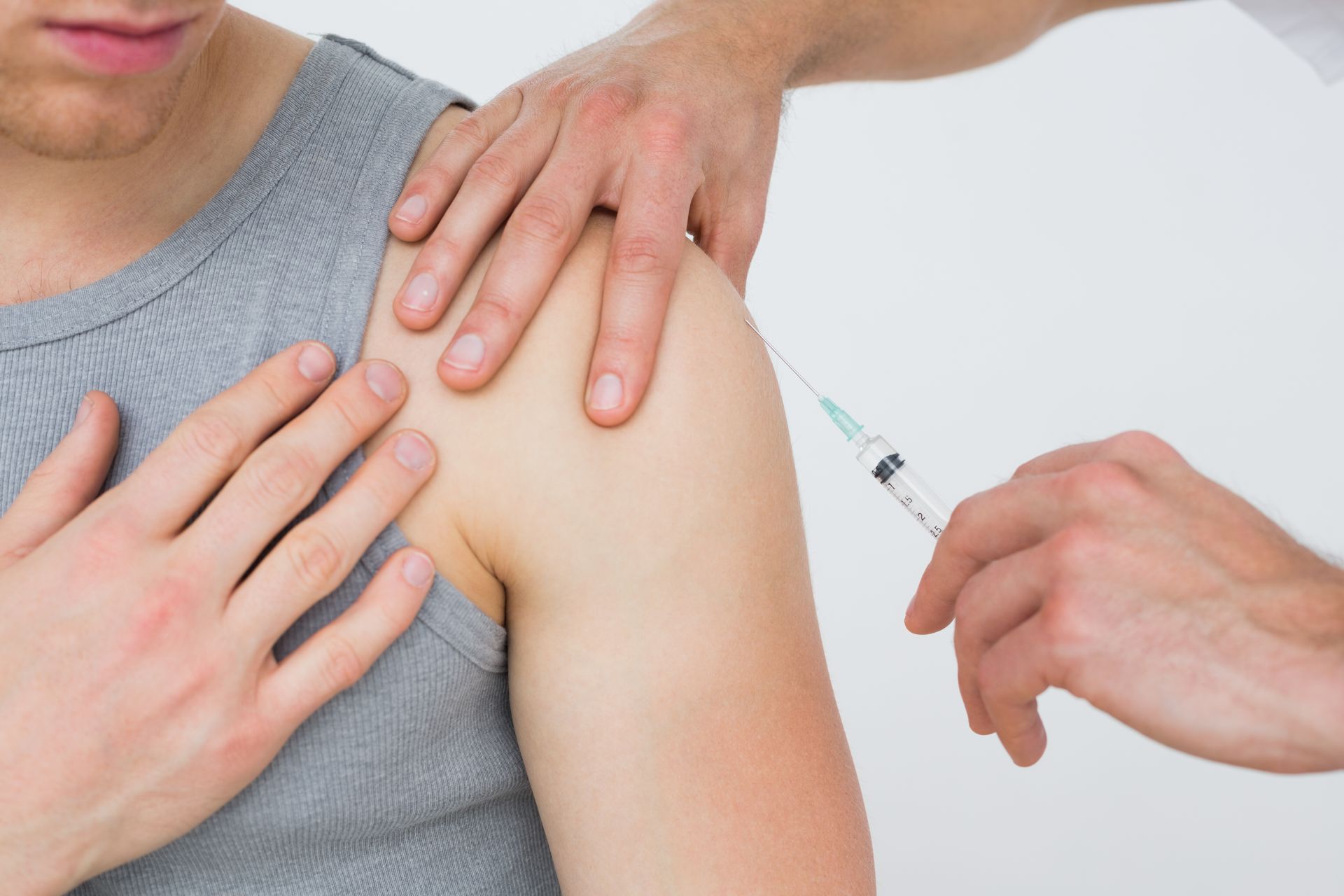 A medical professional administers an injection into a person's shoulder against a plain white background.