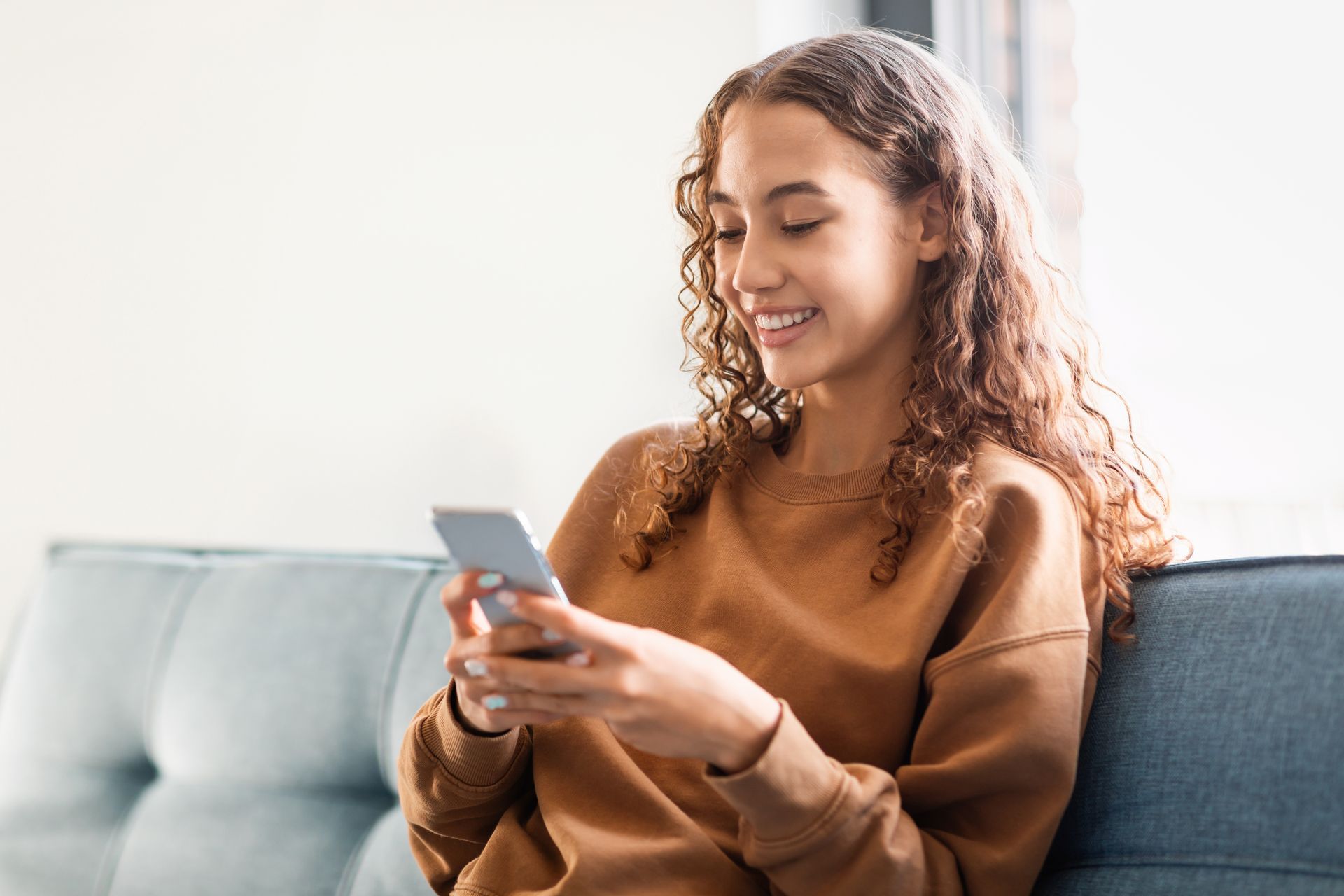 A young woman is sitting on a couch looking at her cell phone.