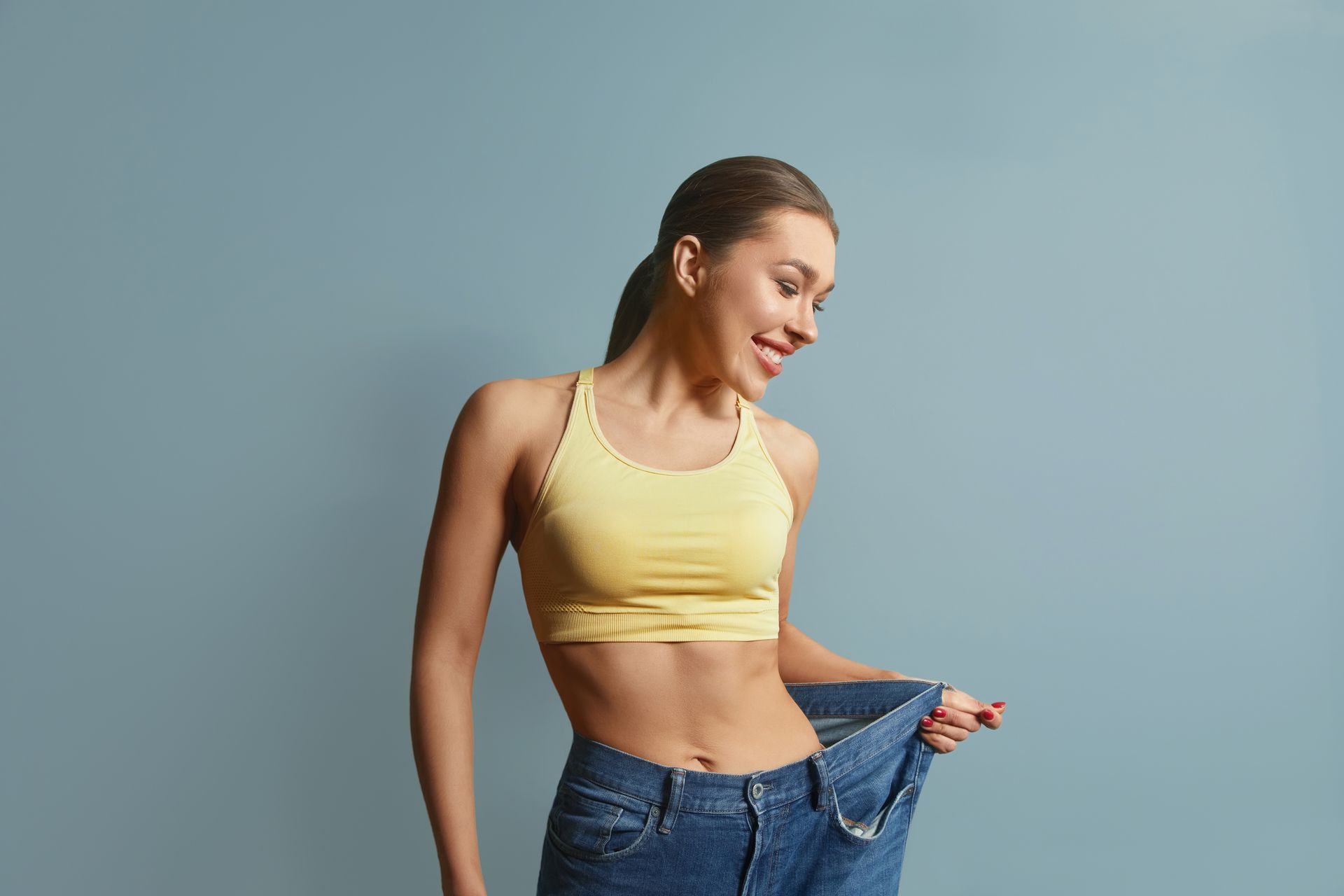 A woman is wearing a yellow sports bra and blue jeans.