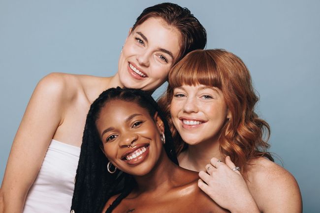 Three women of different races are posing for a picture together and smiling.