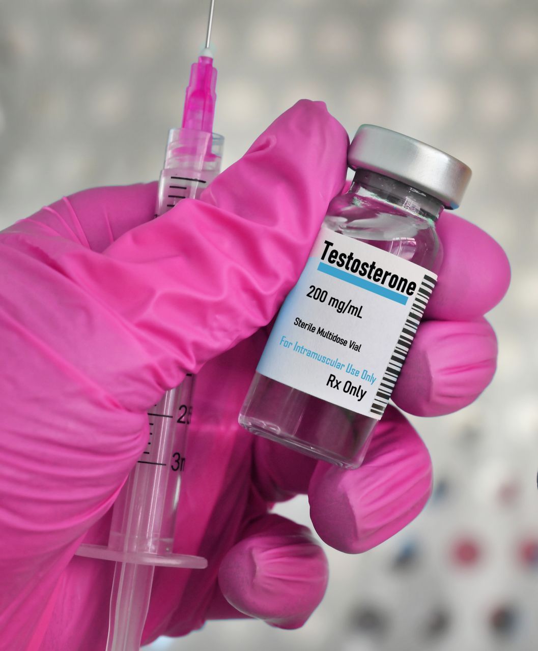 A pink glove is holding a bottle of testosterone and a syringe