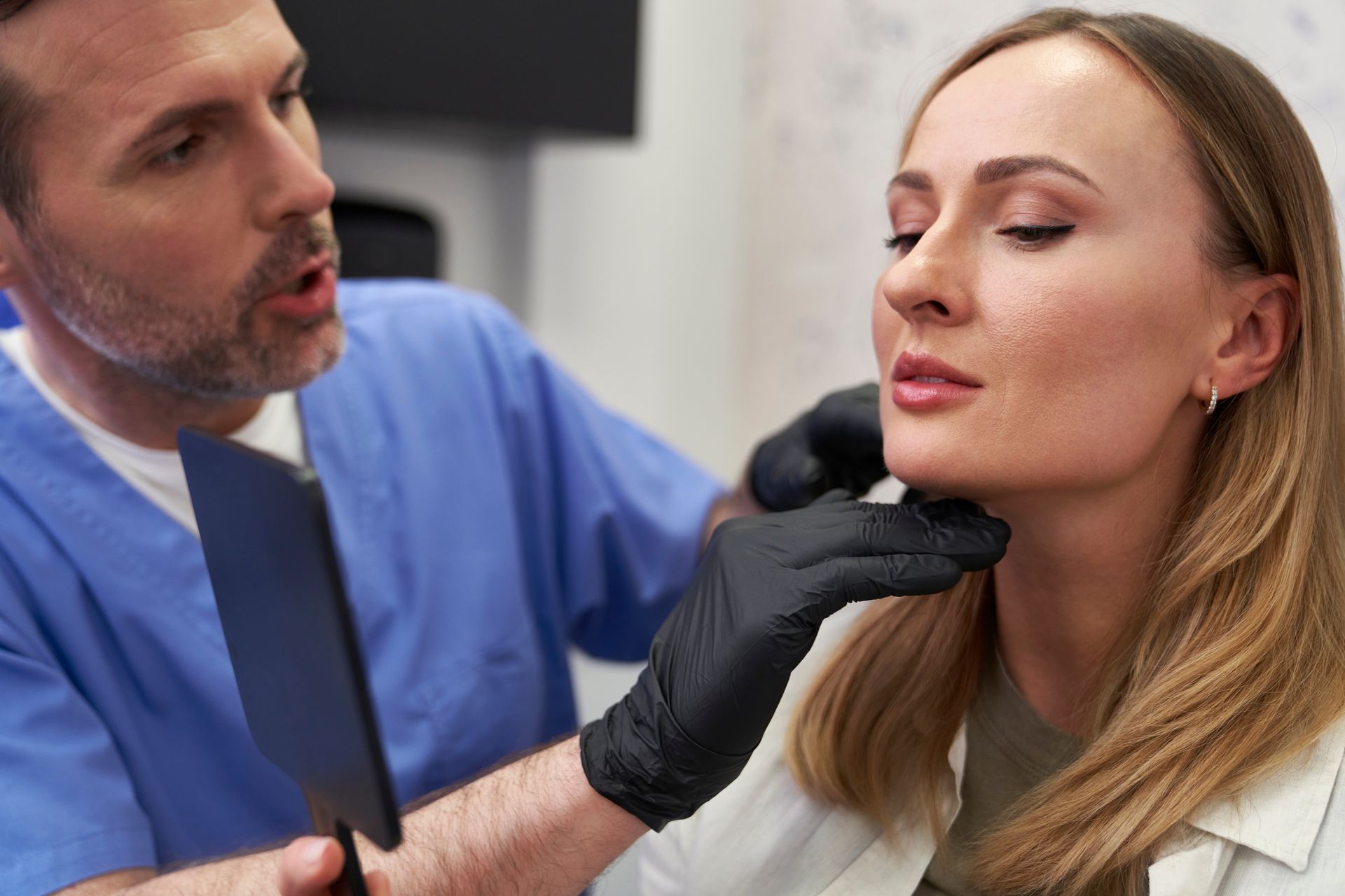 A doctor is examining a woman 's neck with a mirror.