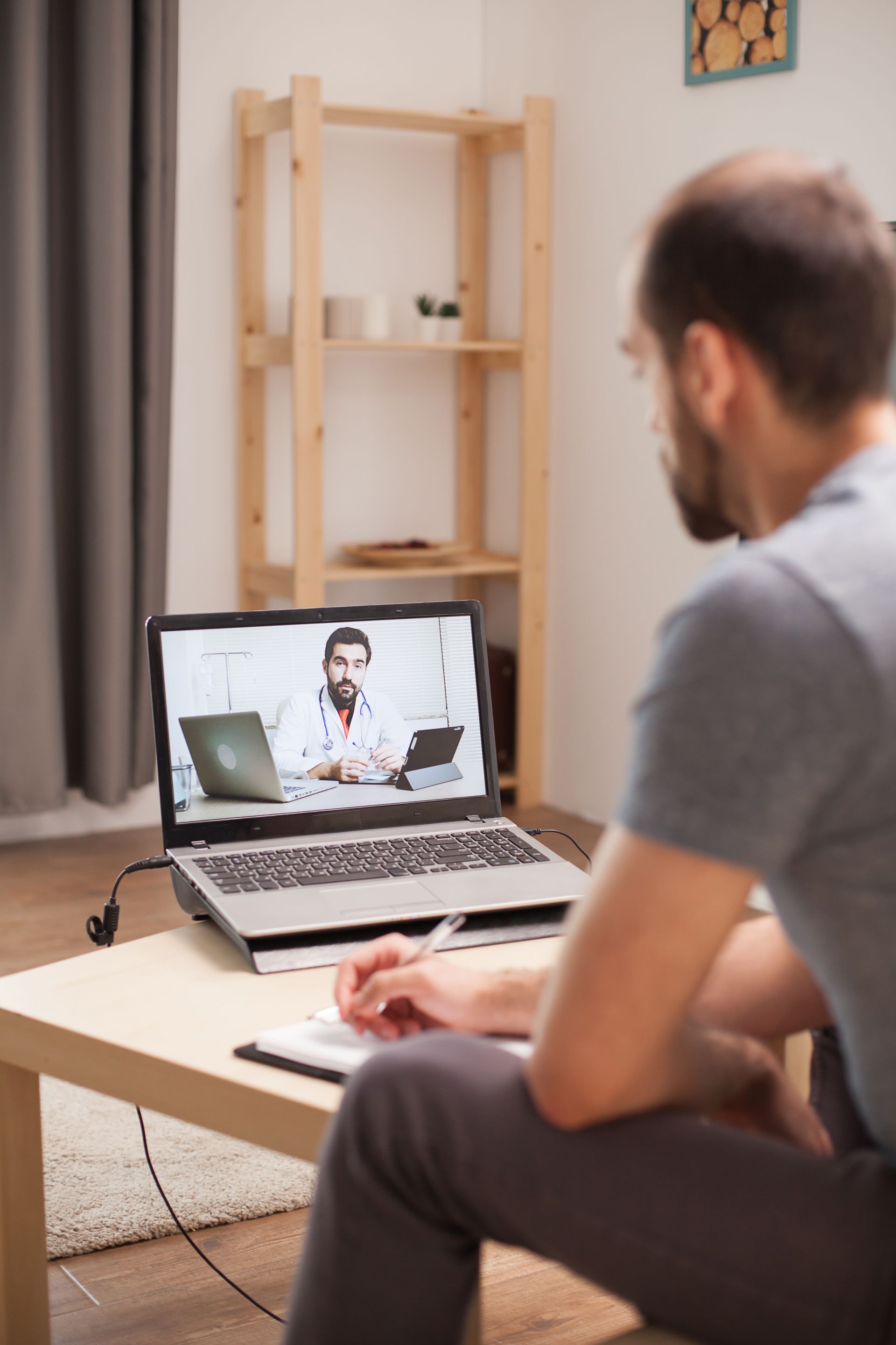 A man is sitting in front of a laptop computer talking to a doctor.
