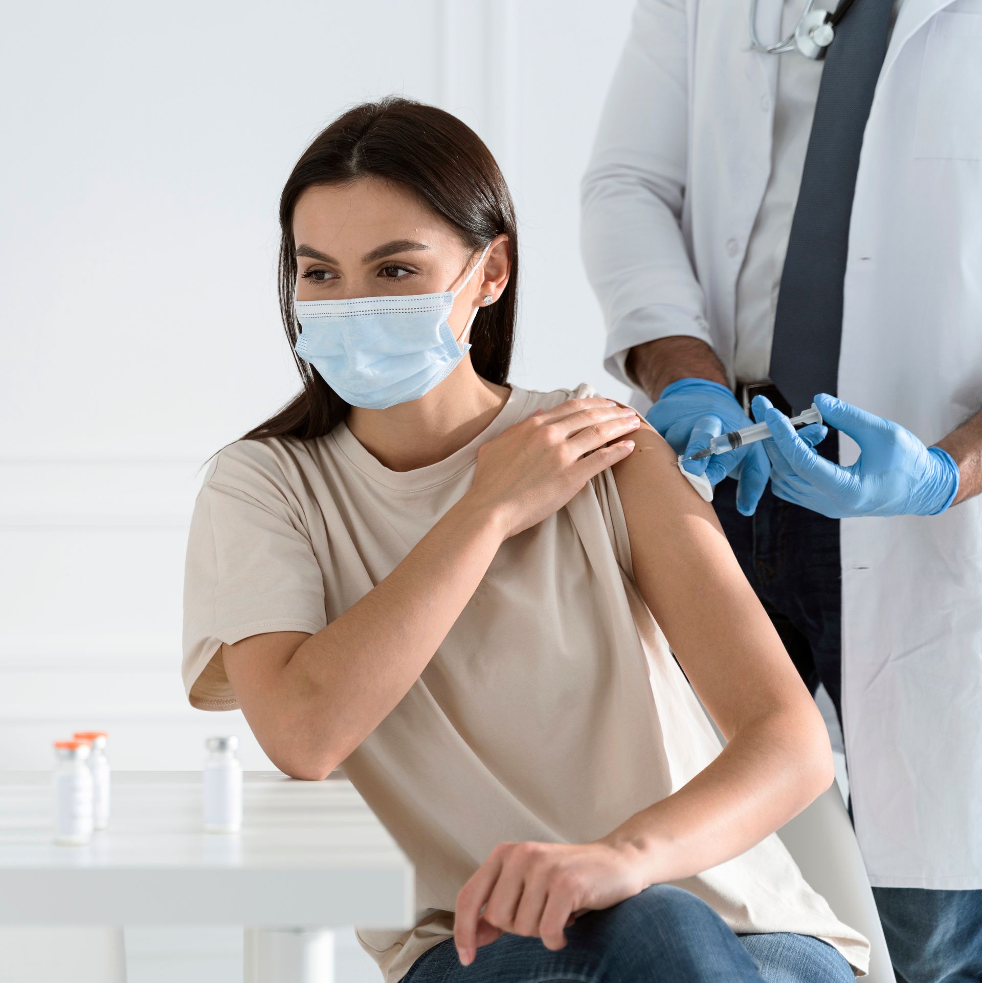 A woman wearing a mask is getting a vaccine from a doctor.