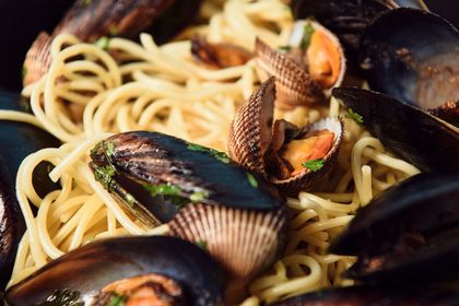 Un primo piano di spaghetti serviti con cozze e vongole fresche nel loro guscio, guarniti con erbe aromatiche.