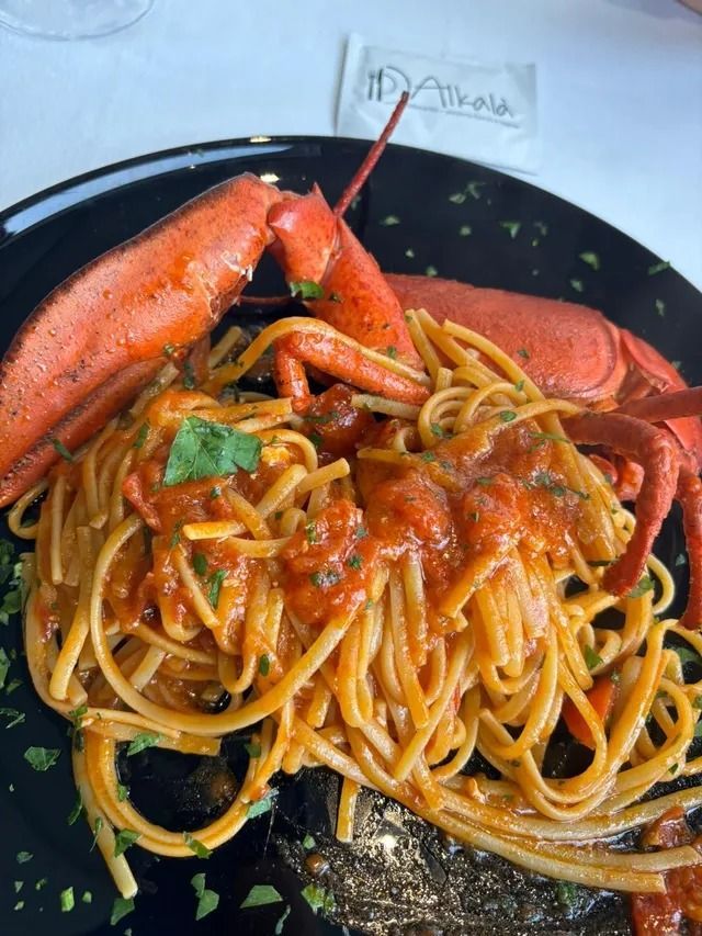 Un piatto di pasta all'astice con salsa di pomodoro, guarnito con erbe fresche, servito su un piatto nero.