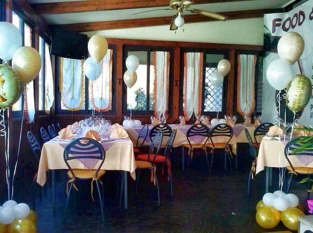 Sala da pranzo decorata con palloncini bianchi e dorati, con tavoli apparecchiati per un evento sotto travi di legno a vista.