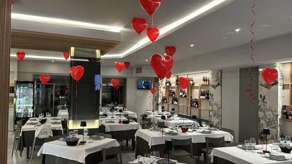 La sala da pranzo di un ristorante è decorata con palloncini rossi a forma di cuore che fluttuano nell'aria, creando un'atmosfera romantica.