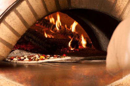Una pizza che cuoce all'interno di un rustico forno a legna in mattoni, con fiamme vivaci sullo sfondo.