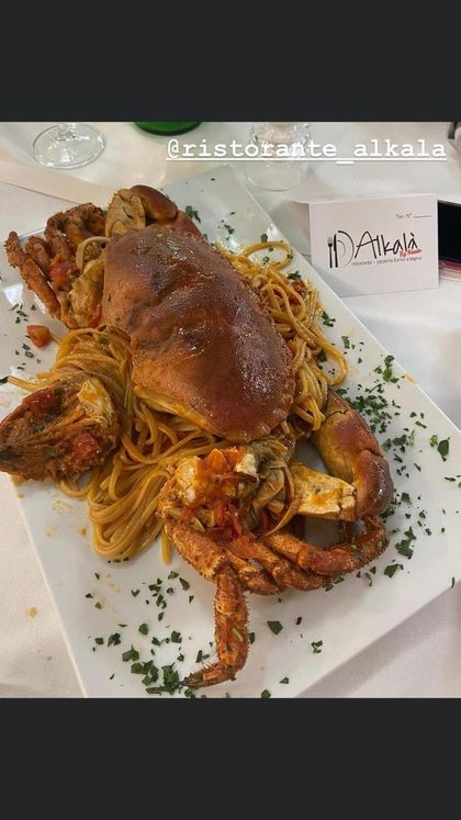 Un grosso granchio cotto servito su un letto di pasta in un piatto bianco, guarnito con erbe aromatiche, in un ristorante.
