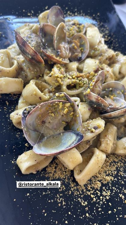Un piatto di pasta ai calamari e vongole, guarnito con pistacchi tritati, su sfondo nero.