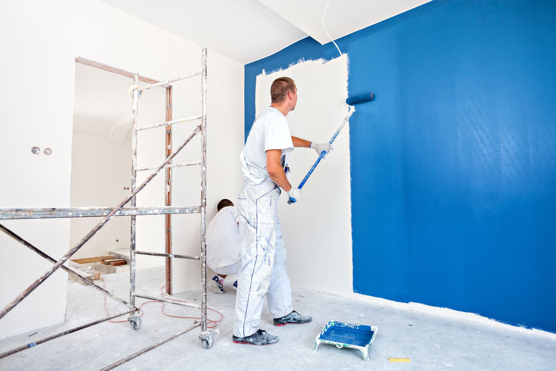 Two men are painting a blue wall in a room.