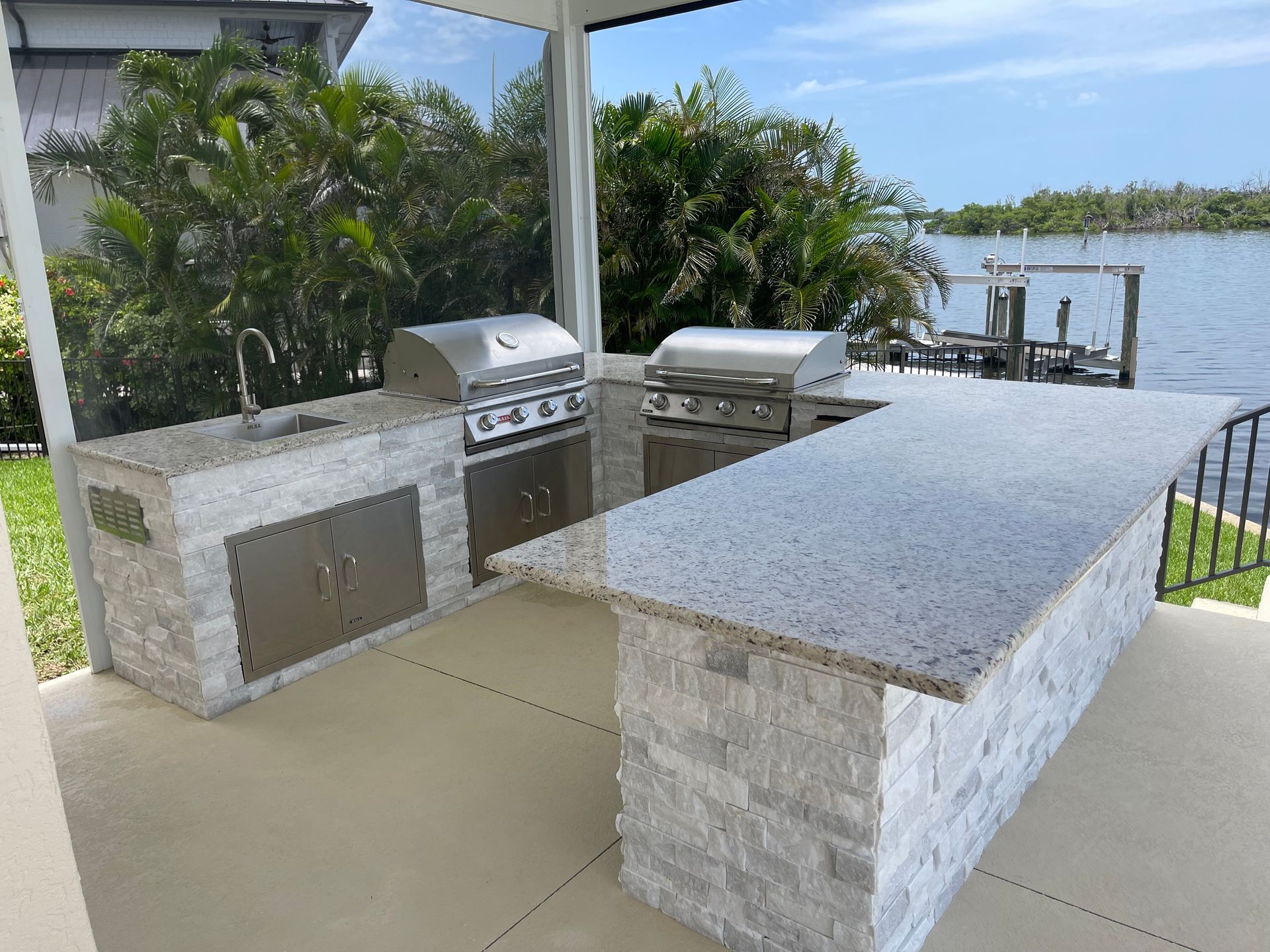 Outdoor kitchen with granite countertops, stainless steel appliances, waterfront view.