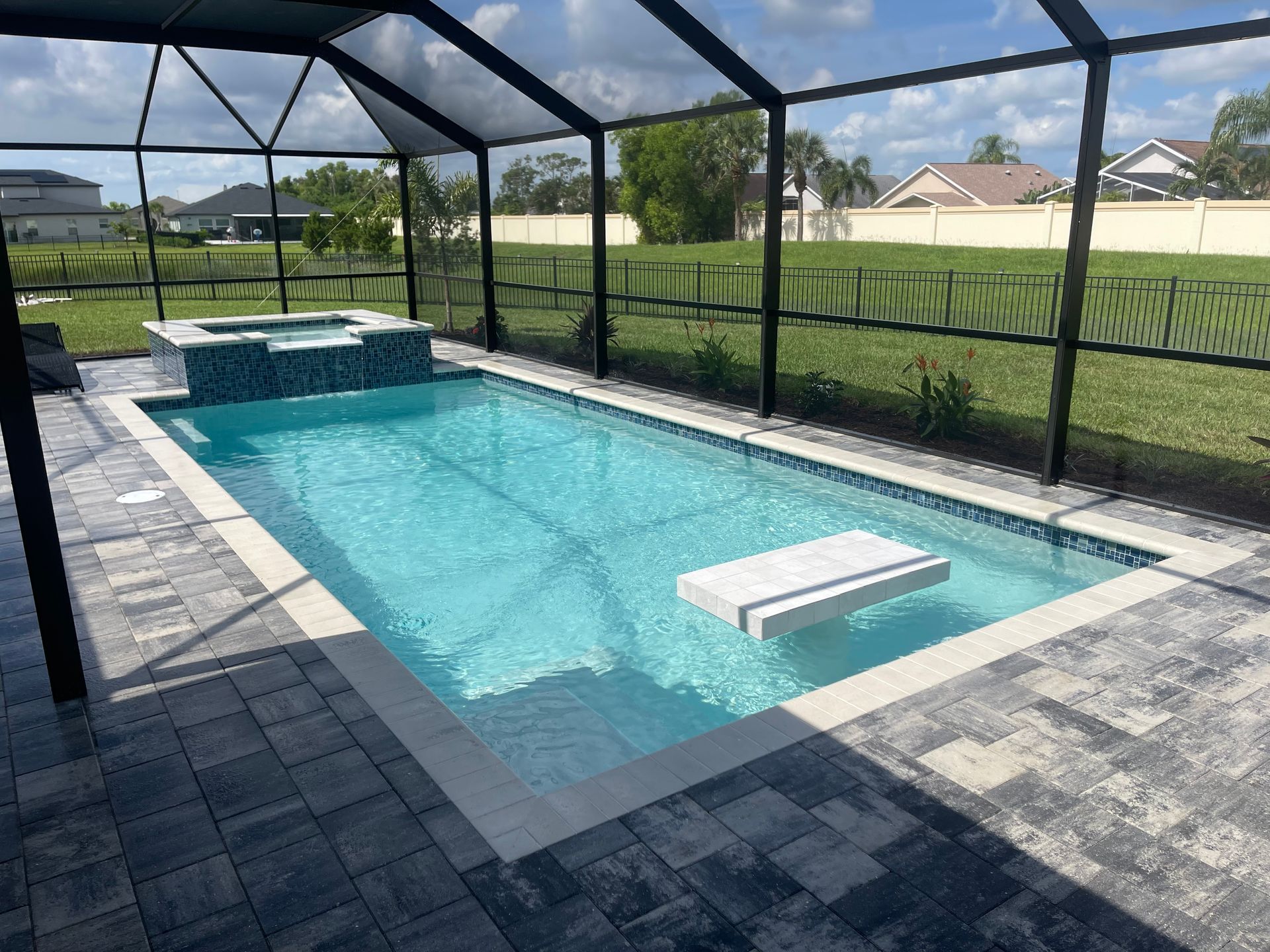 Swimming pool and hot tub in a screened-in patio. Blue water, gray tile, lush green grass in the background.