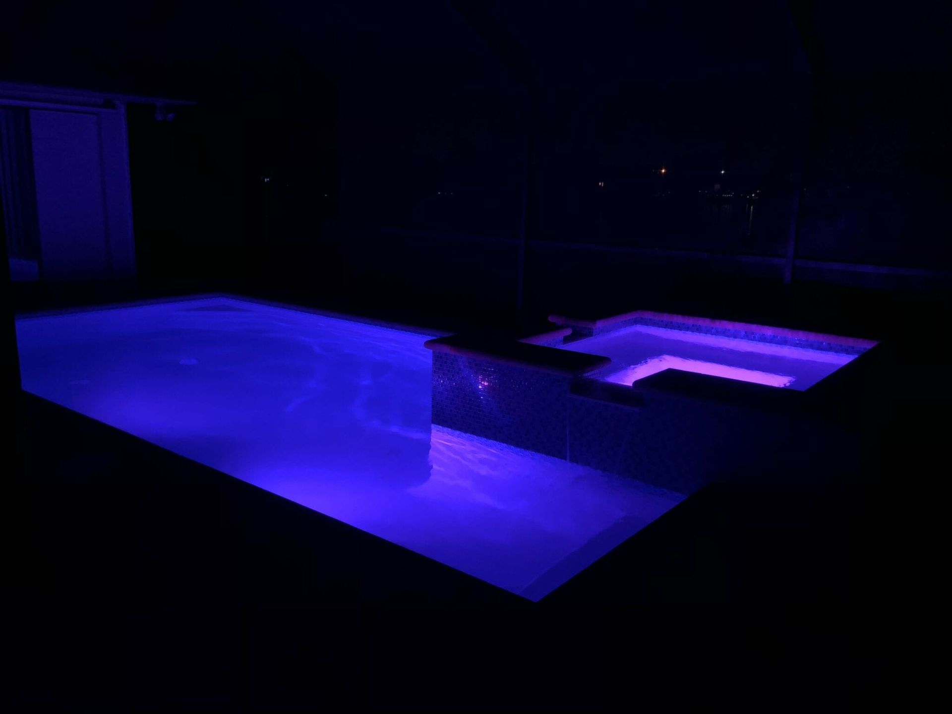 A swimming pool is lit up with blue lights at night.