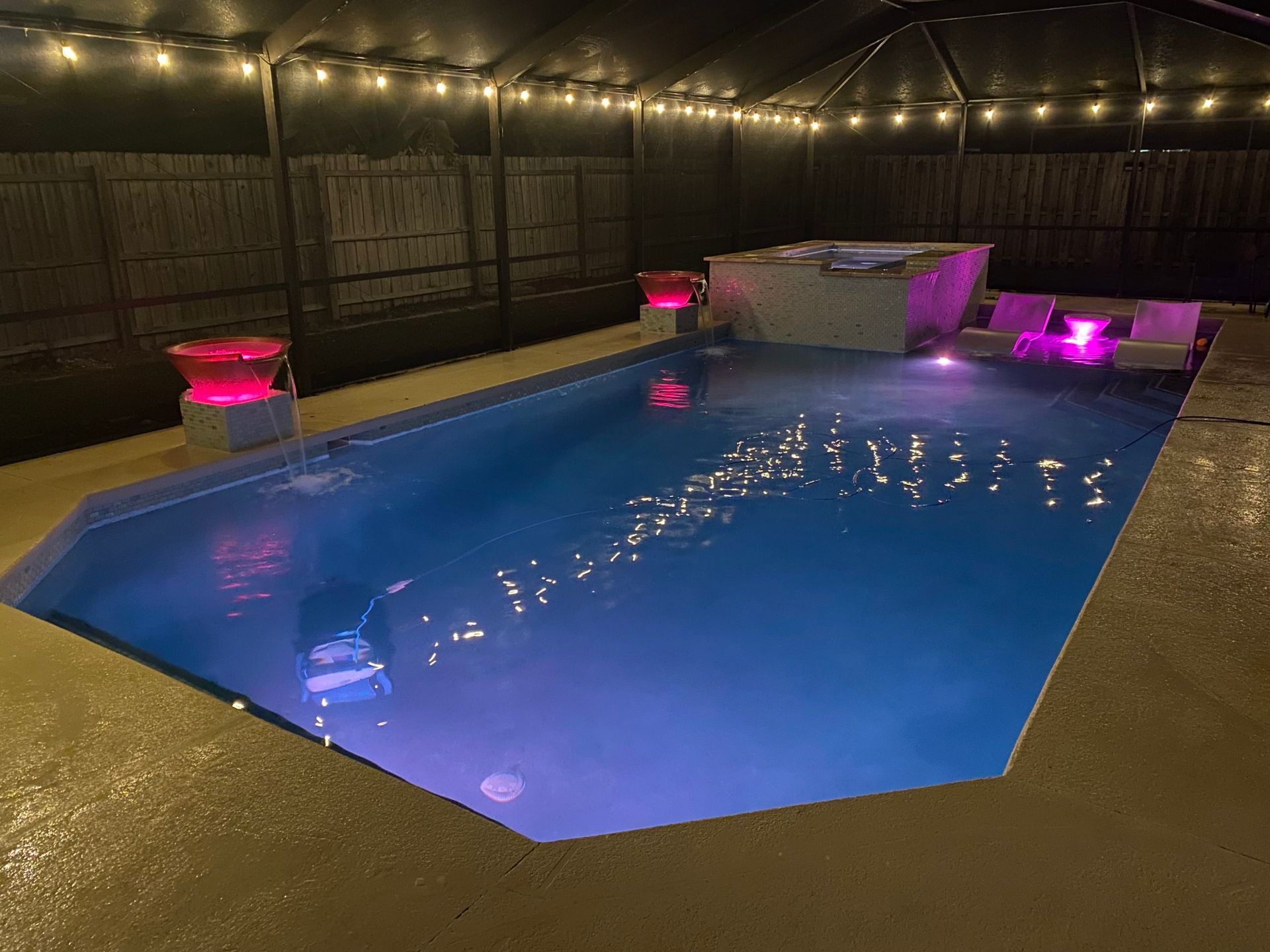 A large swimming pool is lit up at night with purple lights.