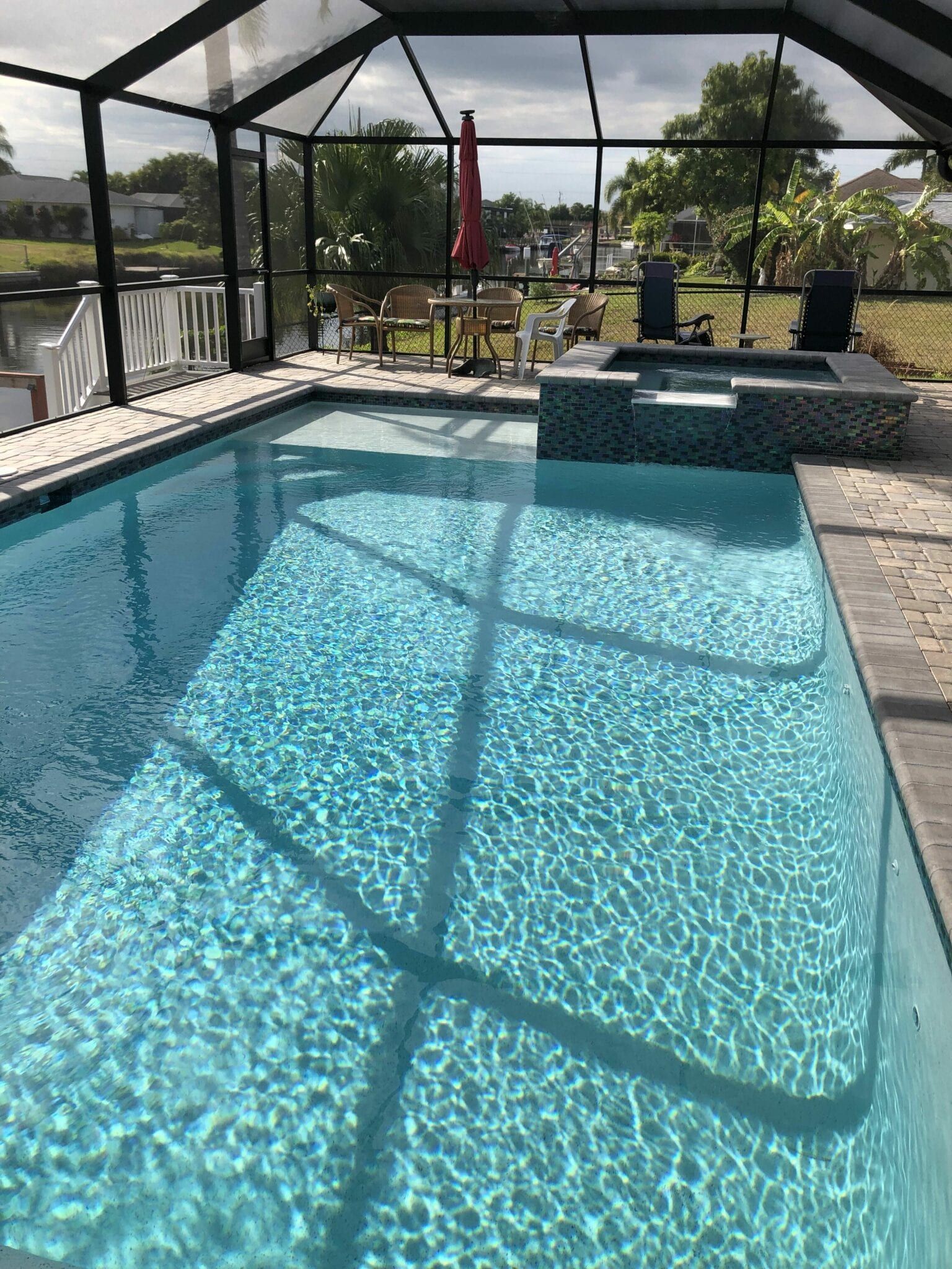 A large swimming pool covered in a screened in area with chairs and umbrellas.