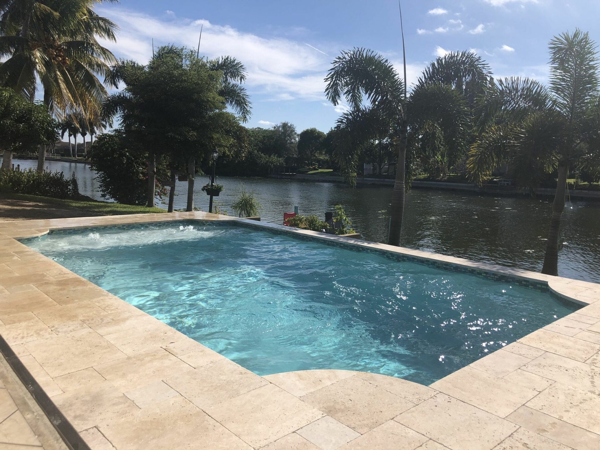 A large swimming pool surrounded by palm trees and a body of water built by Into h2o Pools & Spas Cape Coral