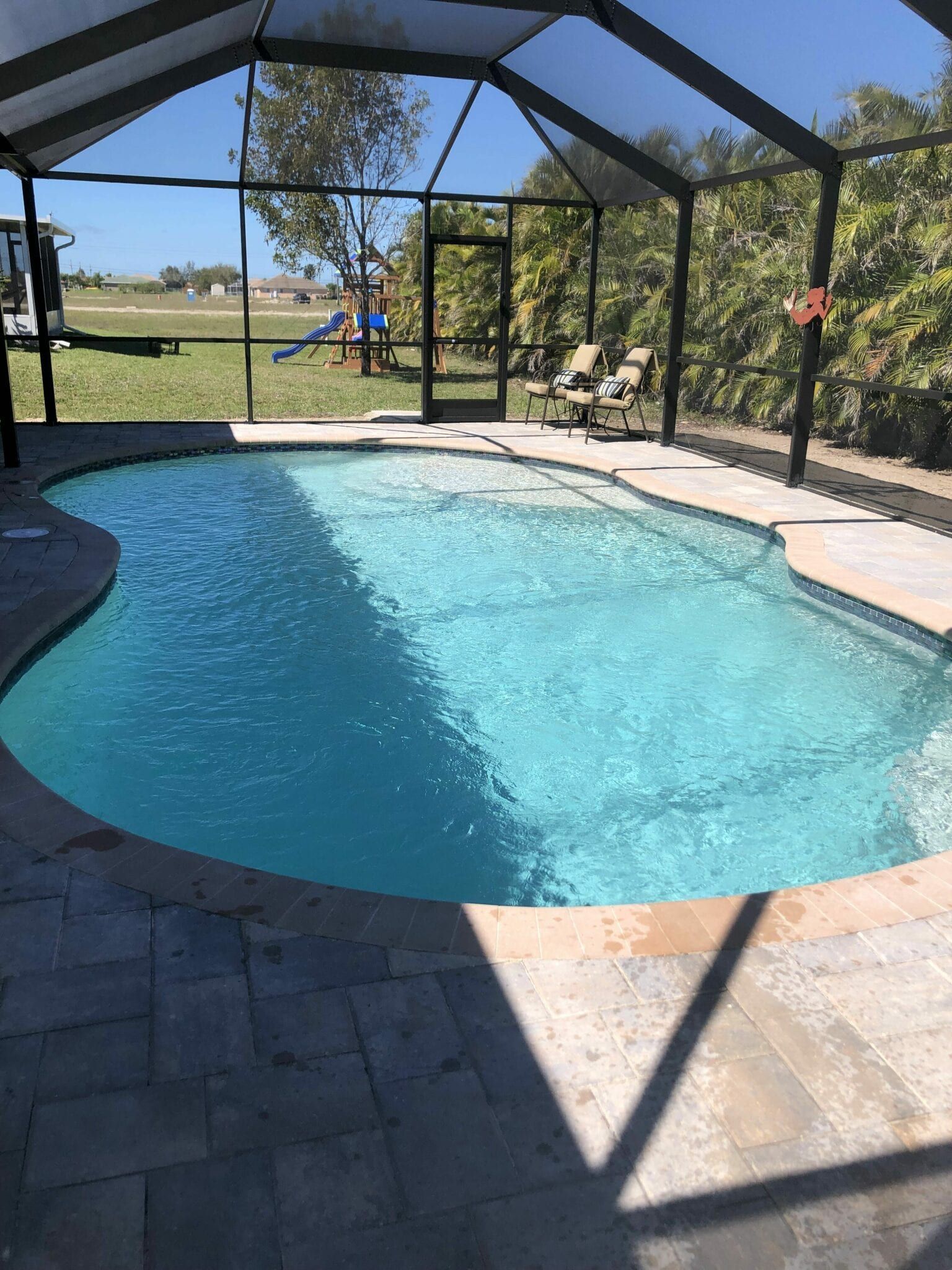 A large swimming pool is surrounded by a screened in area built by Into h2o Pools & Spas Cape Coral