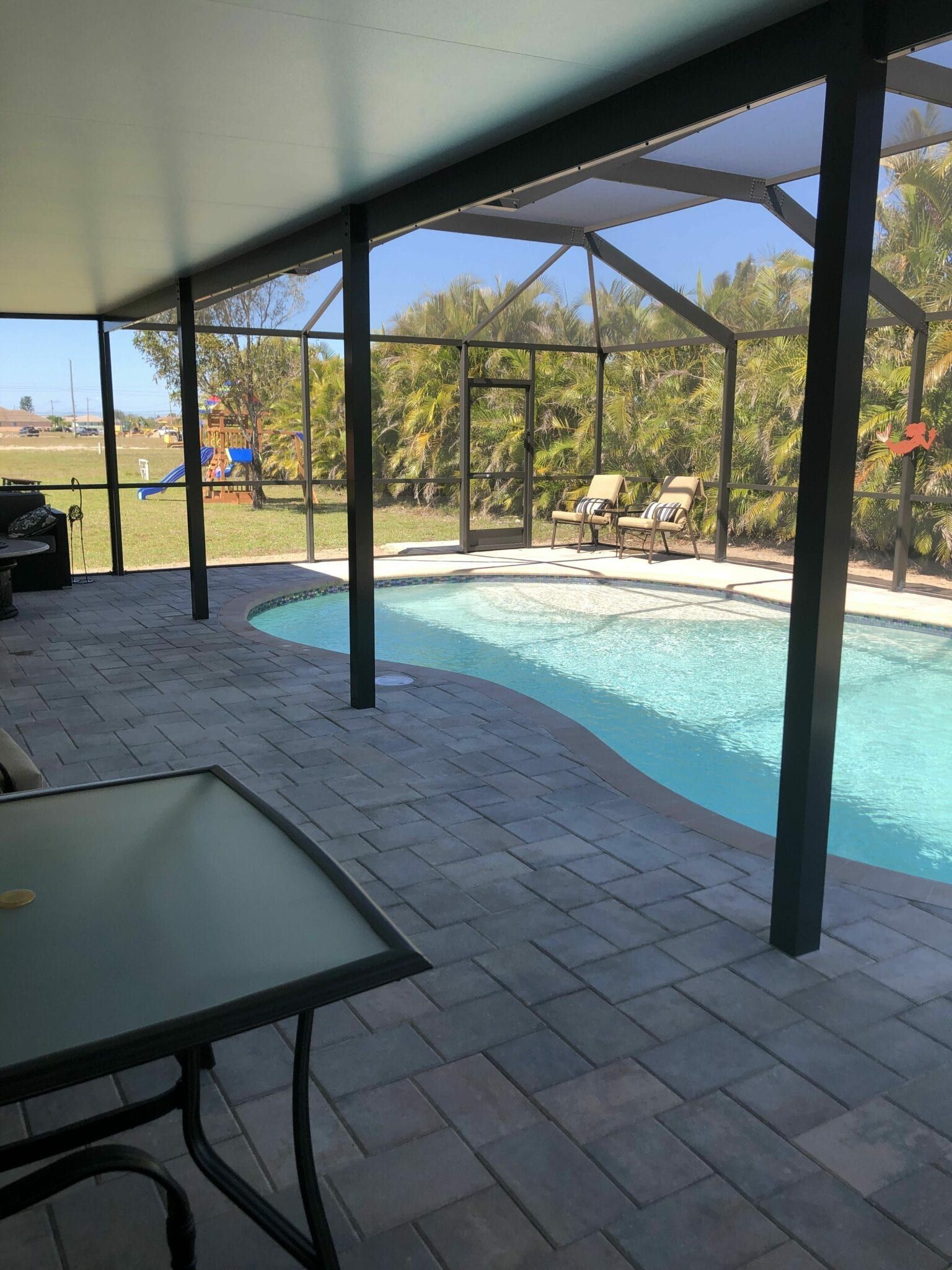 A large swimming pool is surrounded by a screened in area with a table and chairs built by Into h2o Pools & Spas Cape Coral