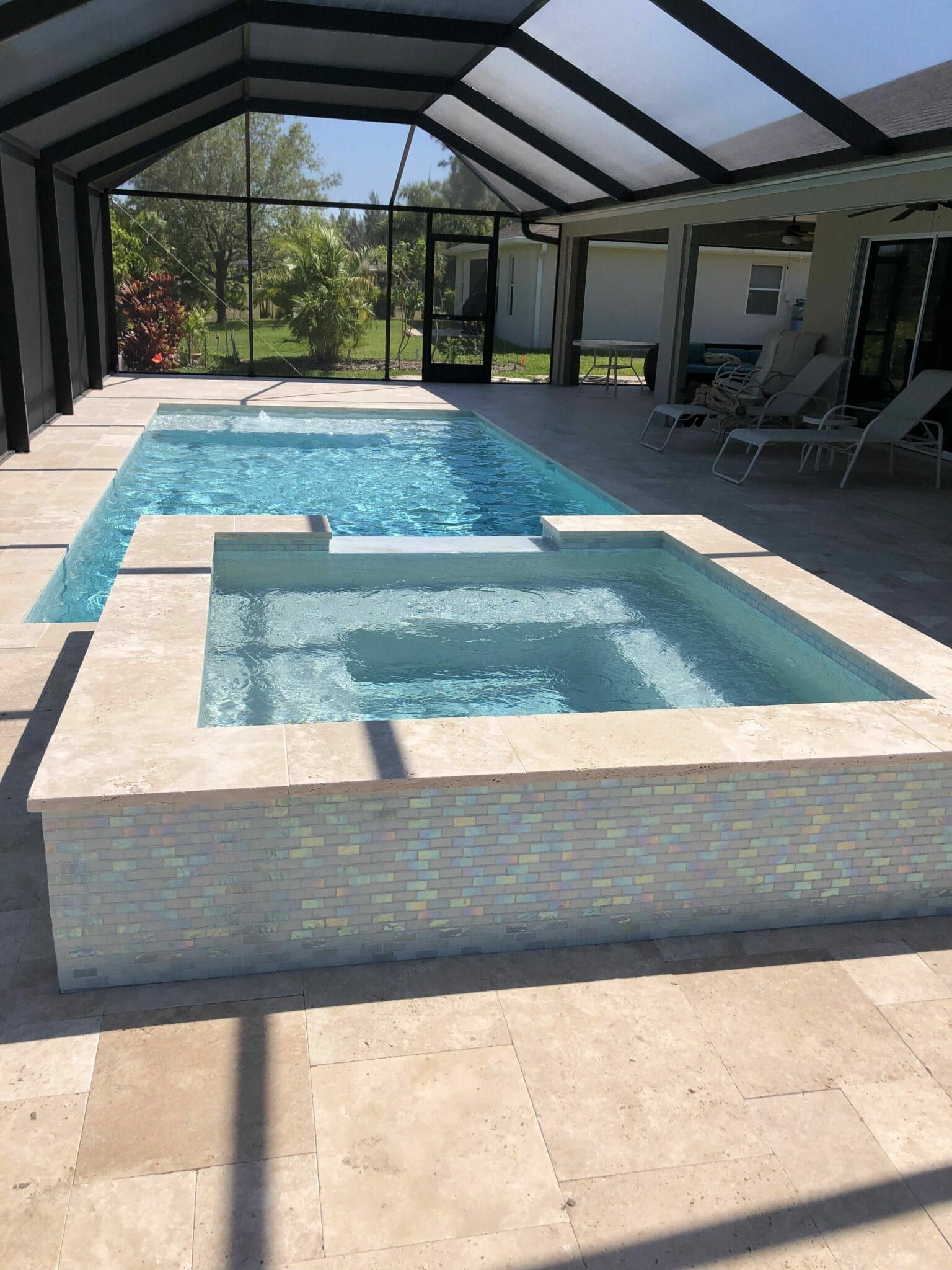 A large indoor swimming pool with a hot tub underneath it built by Into h2o Pools & Spas Cape Coral