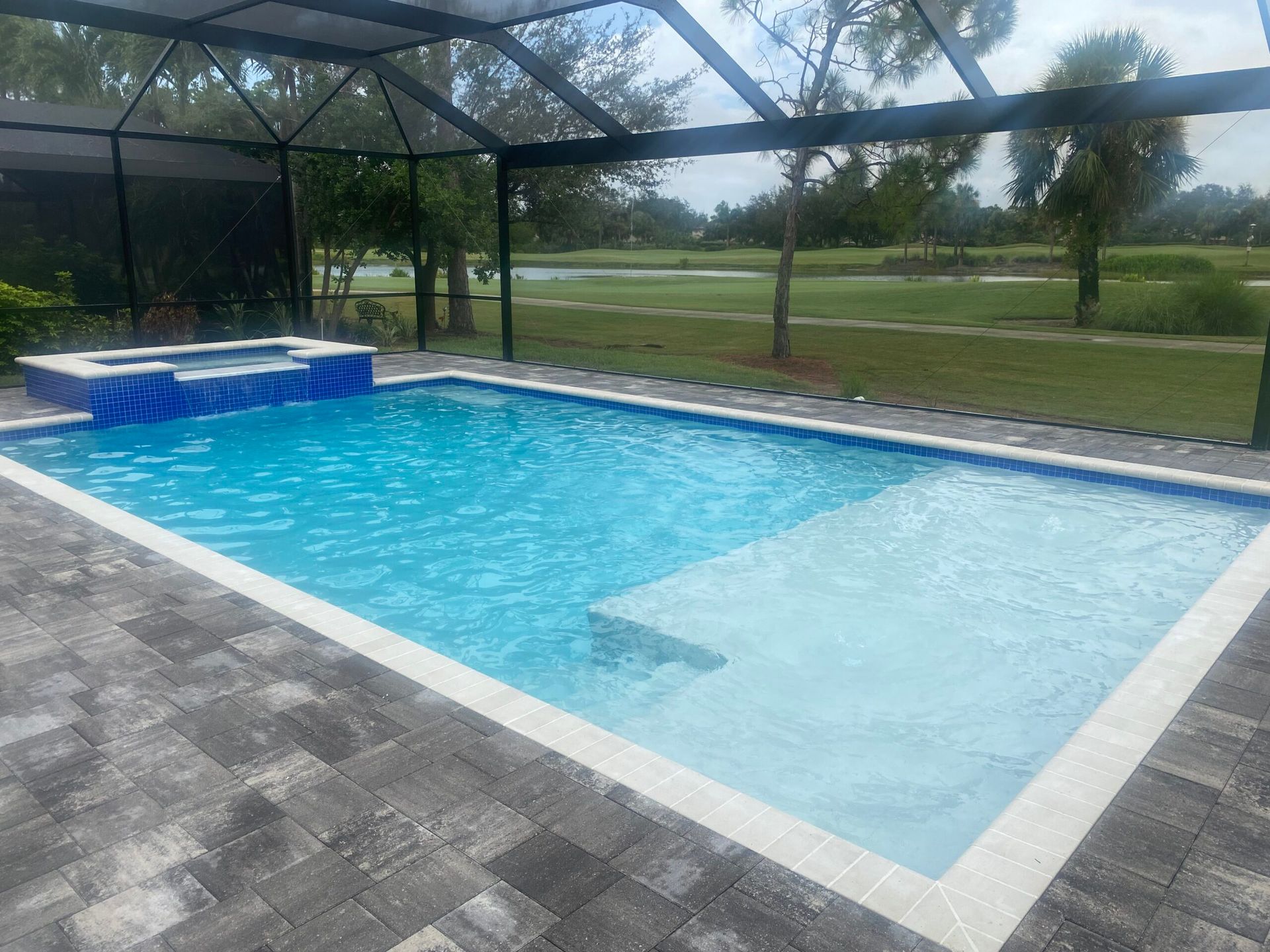 A large swimming pool surrounded by a screened in area built by Into h2o Pools & Spas Cape Coral with a view of a golf course.