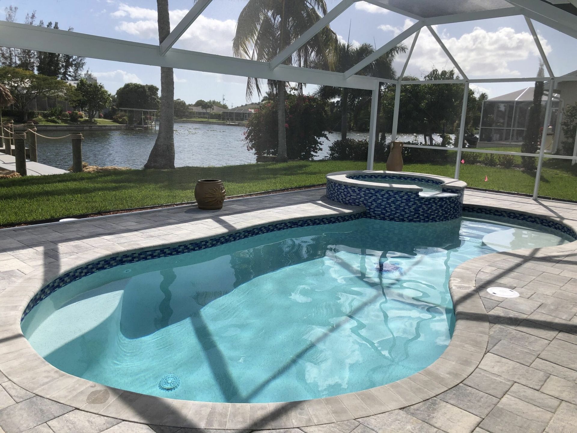 A large swimming pool is surrounded by a screened in area with a view of a lake built by Into h2o Pools & Spas Cape Coral