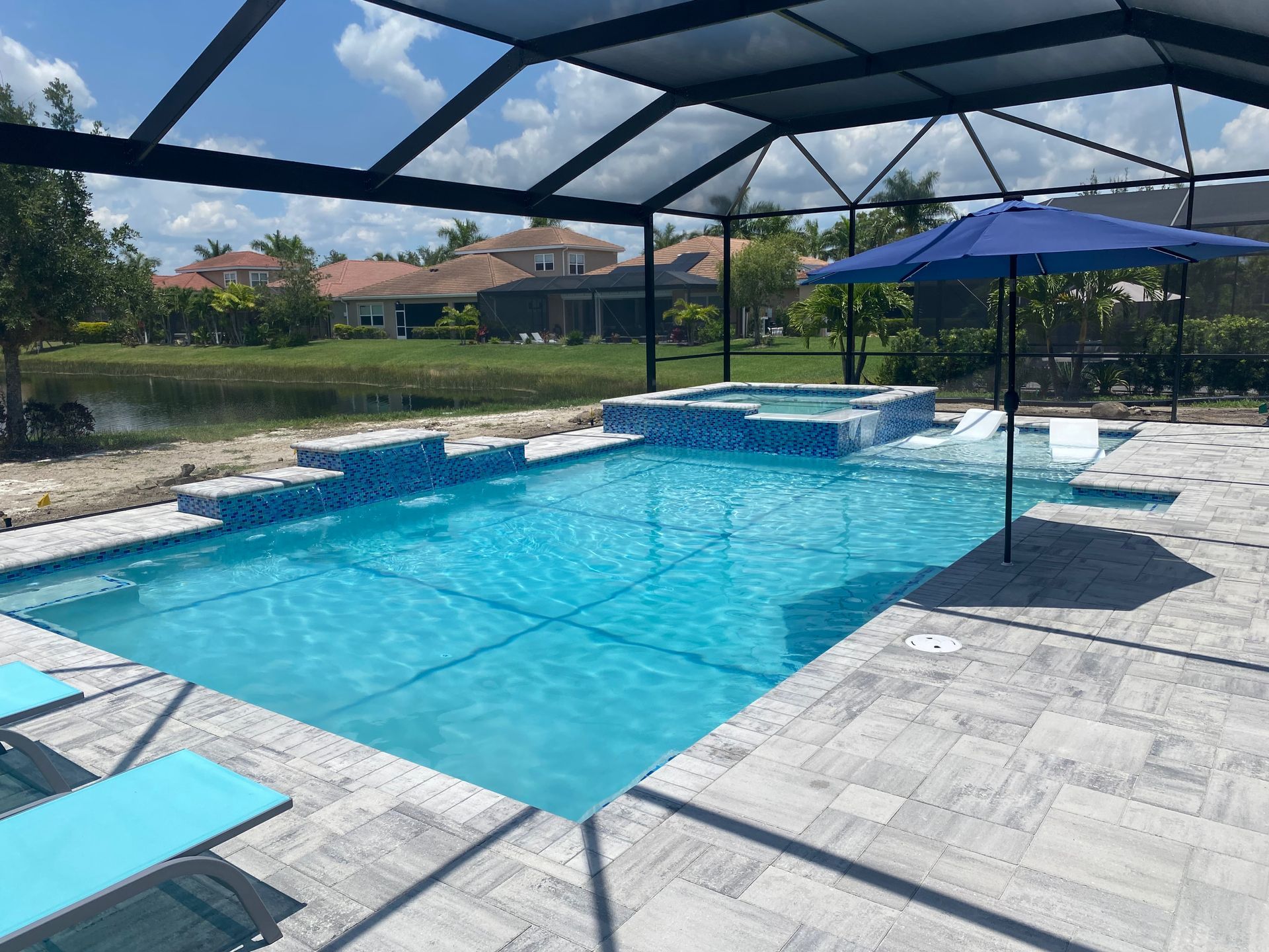 A large swimming pool with a blue umbrella and chairs around it built by Into h2o Pools & Spas Cape Coral