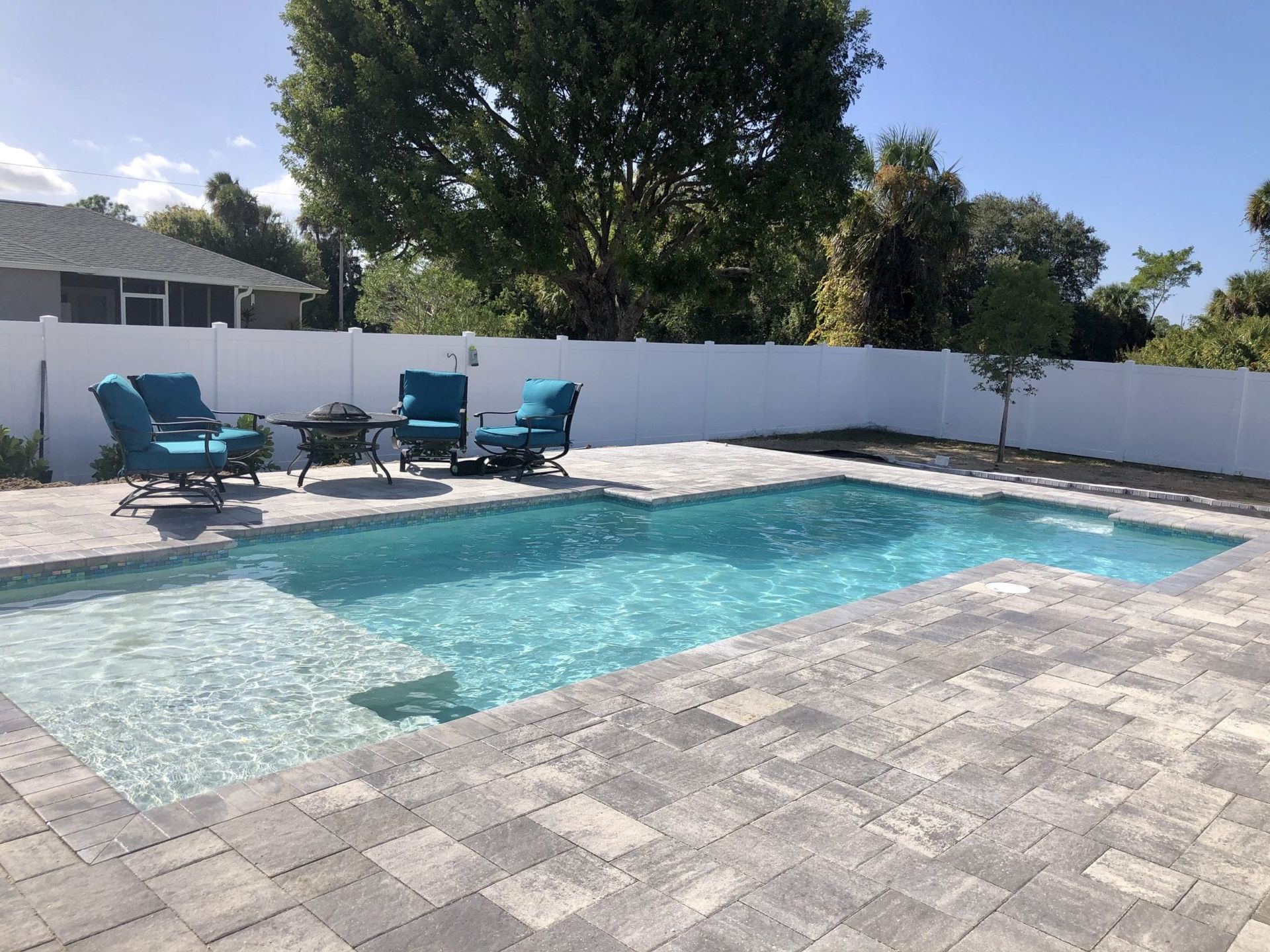 A large swimming pool is surrounded by chairs and a white fence built by Into h2o Pools & Spas Cape Coral