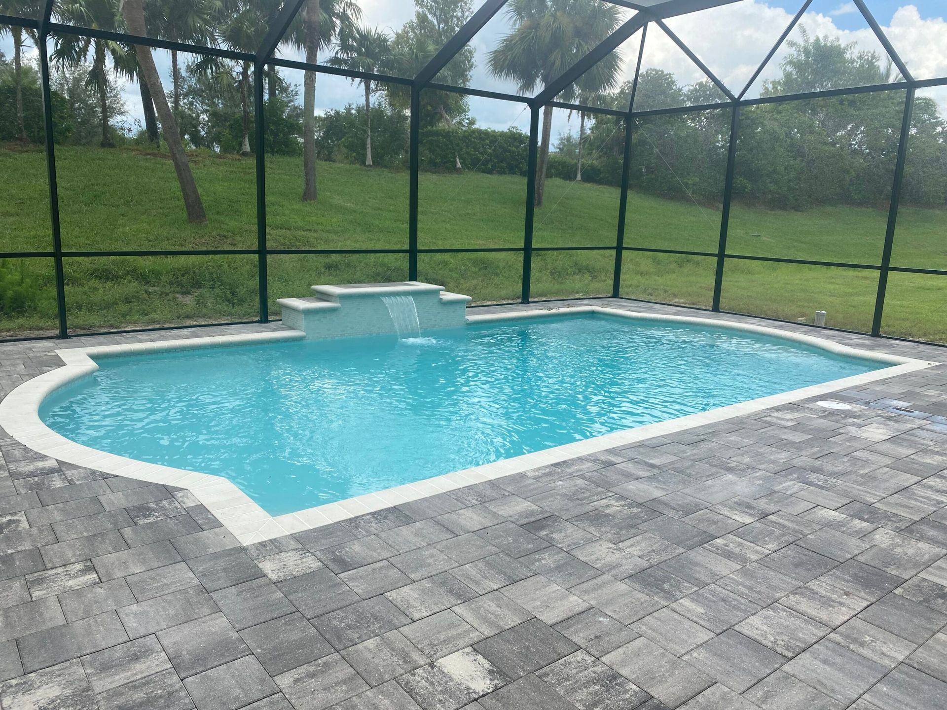 A large swimming pool with a waterfall in the middle built by Into h2o Pools & Spas Cape Coral