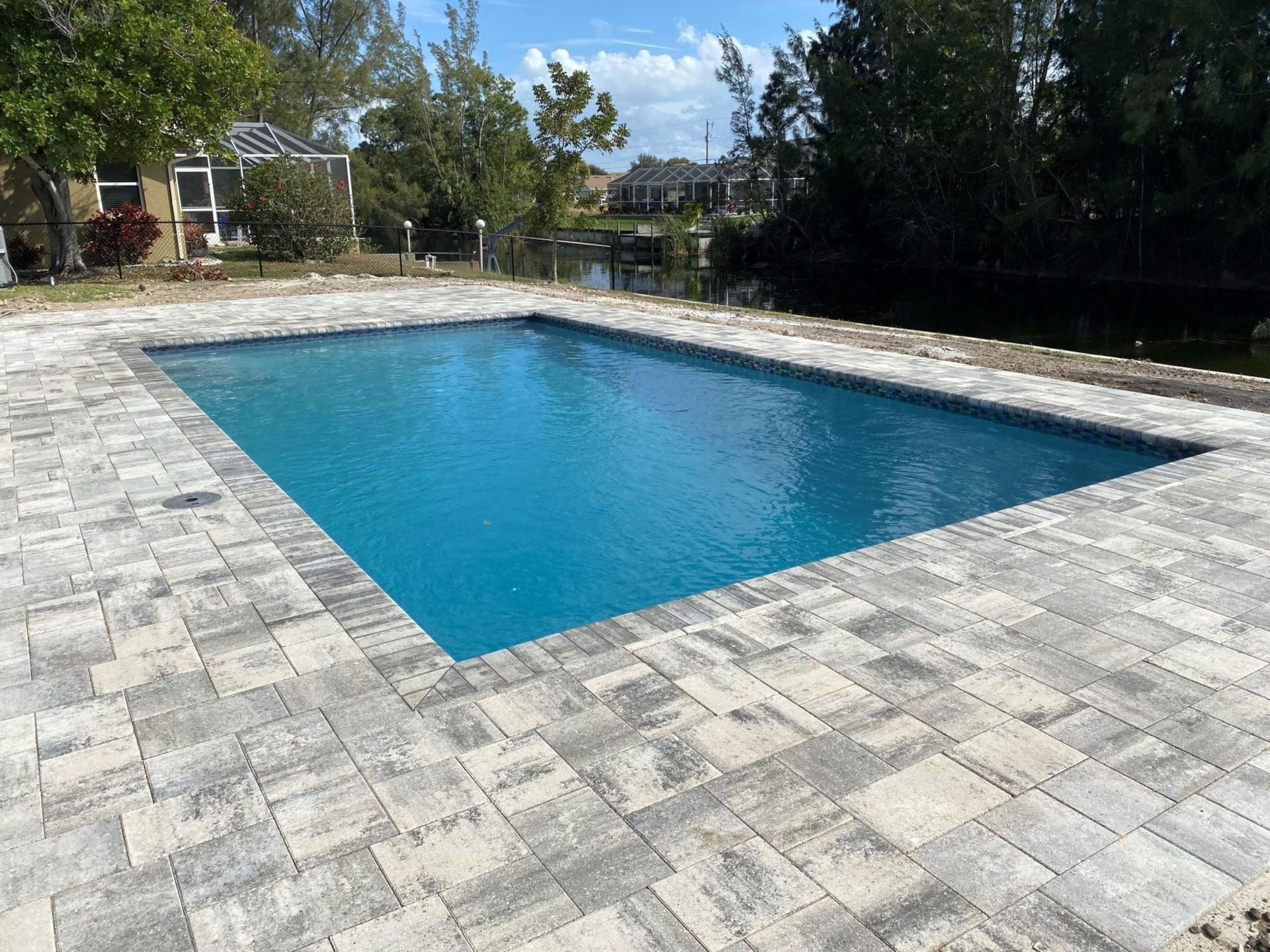 A large swimming pool is surrounded by a brick patio.