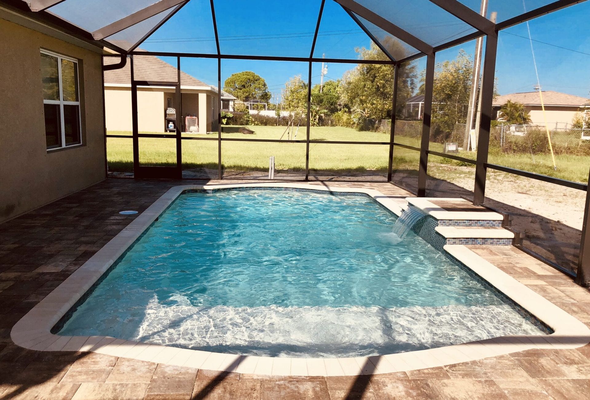 A large swimming pool is surrounded by a screened in area.