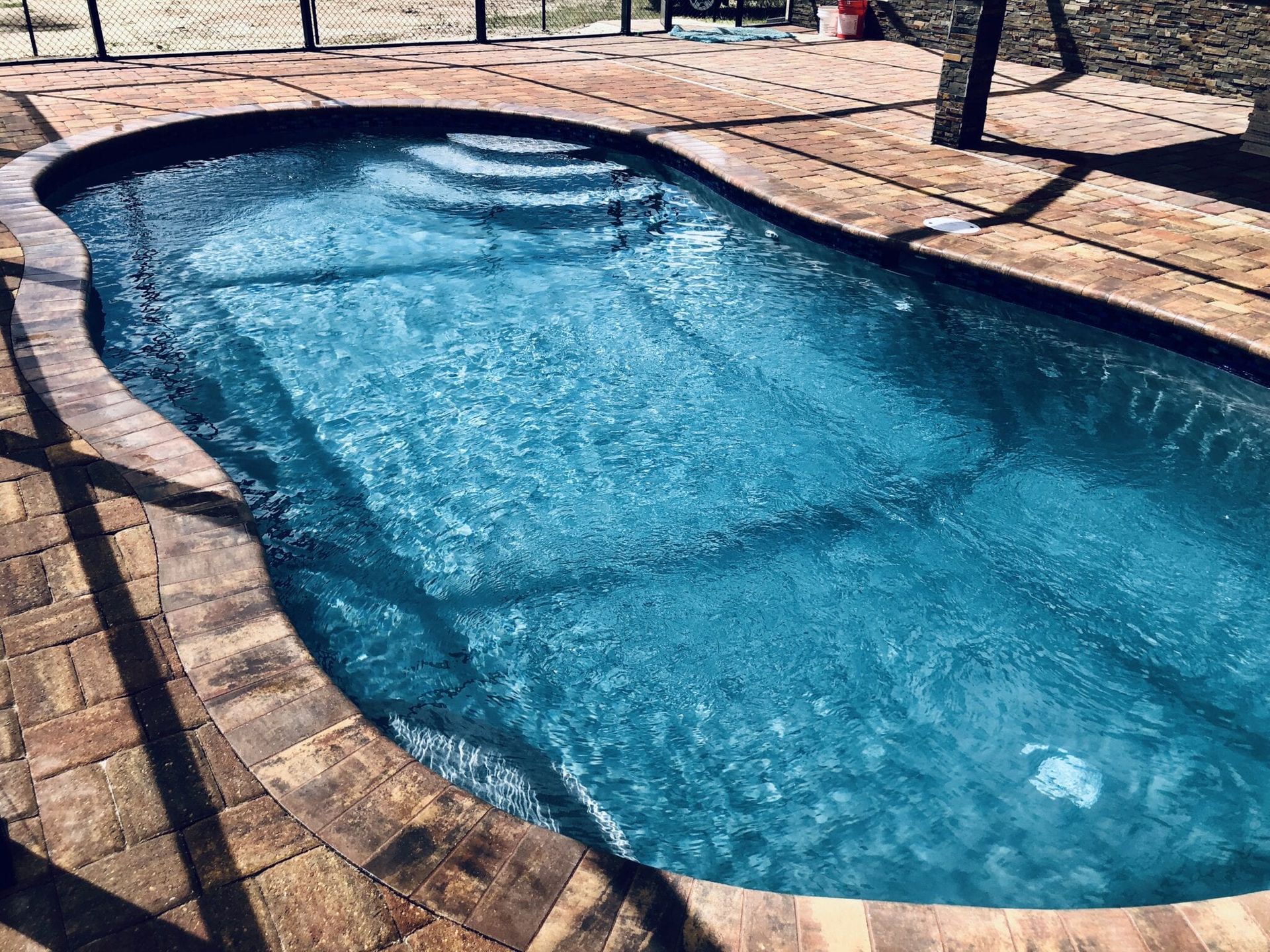 A large swimming pool filled with blue water is sitting on top of a brick patio.