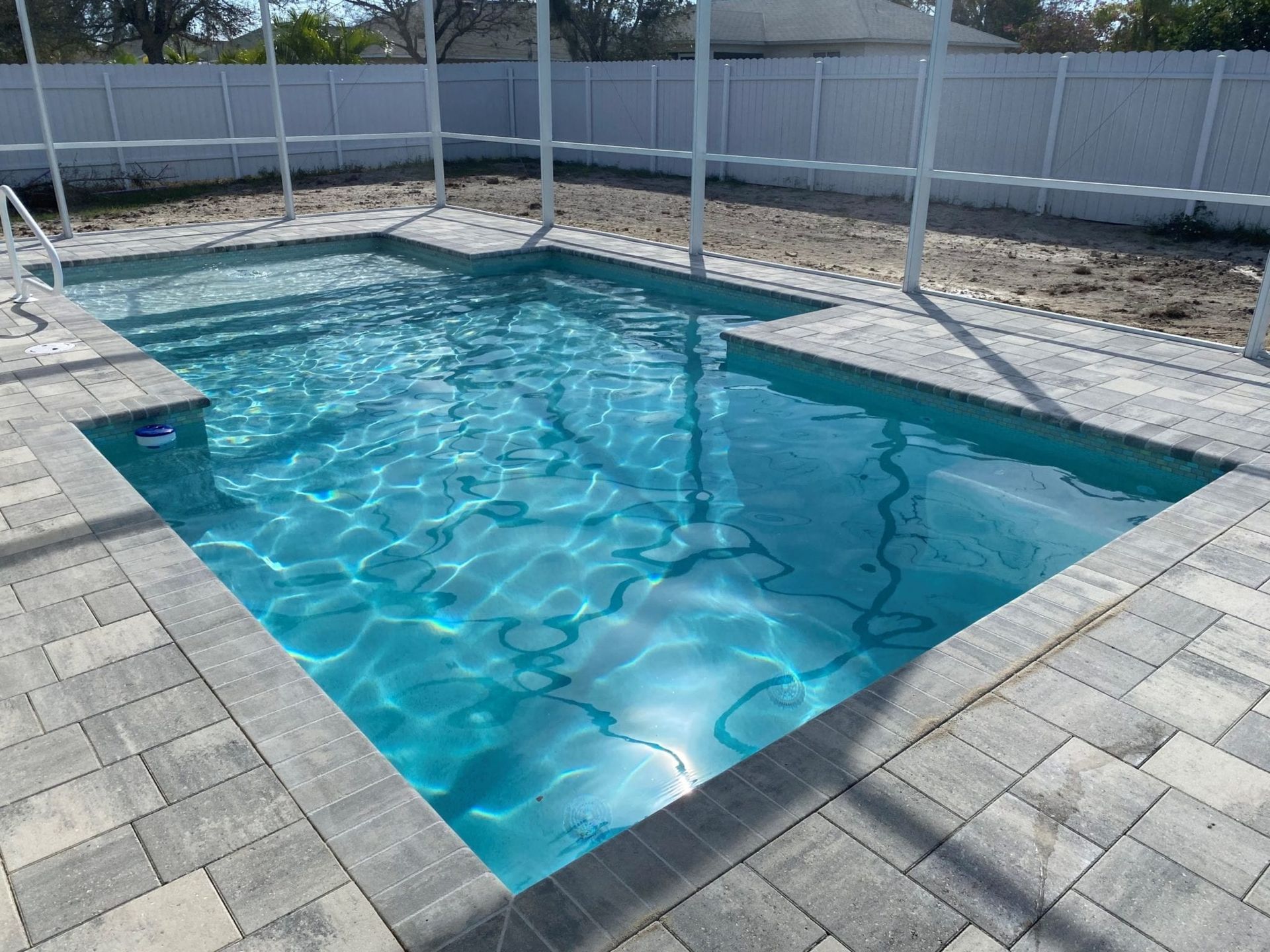 A large swimming pool is surrounded by a brick patio and a white fence built by Into h2o Pools & Spas Cape Coral