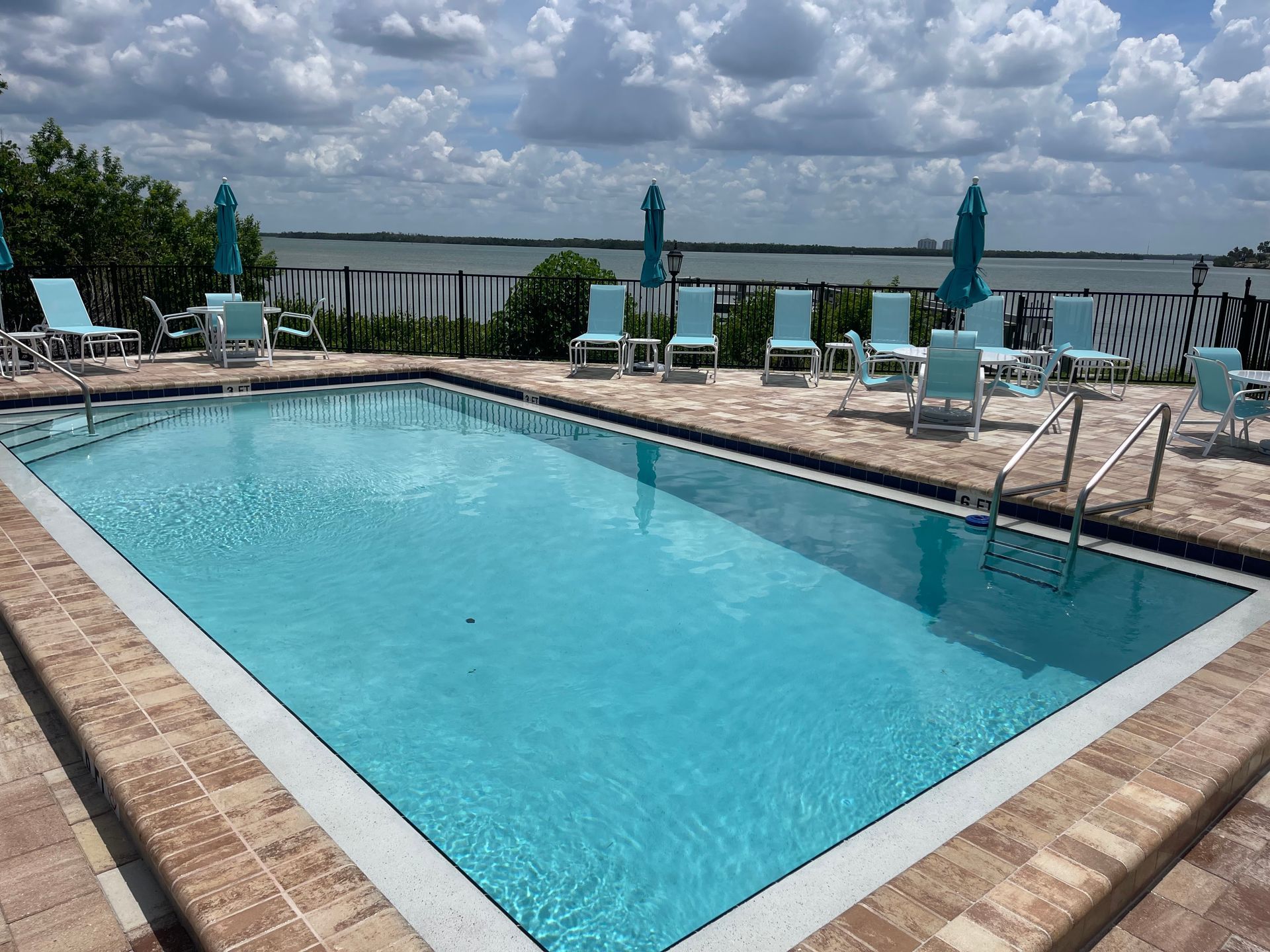 Pool with turquoise water and lounge chairs, waterfront setting, sunny day.