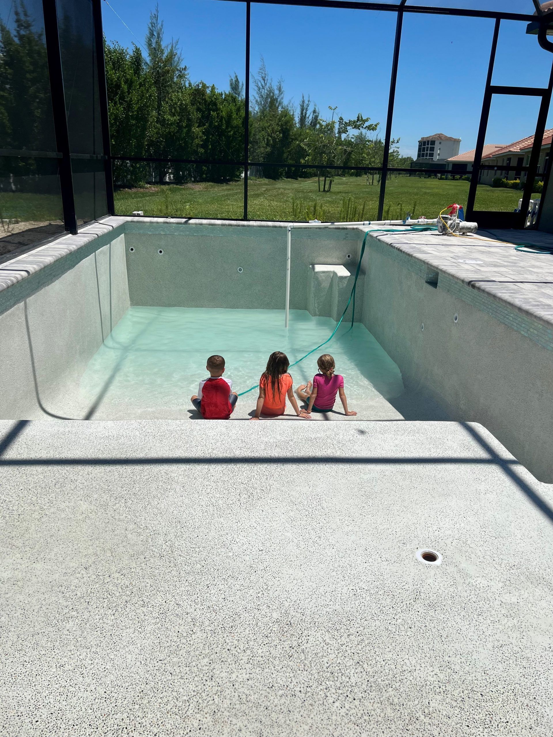 Three children are sitting on the edge of a swimming pool built by Into h2o Pools & Spas Cape Coral