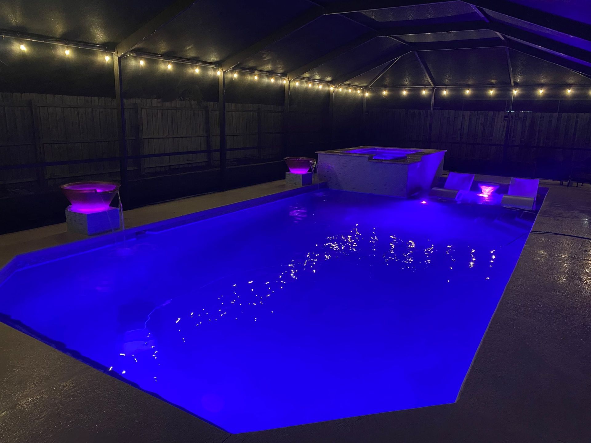 A large swimming pool is lit up with blue lights at night built by Into h2o Pools & Spas Cape Coral