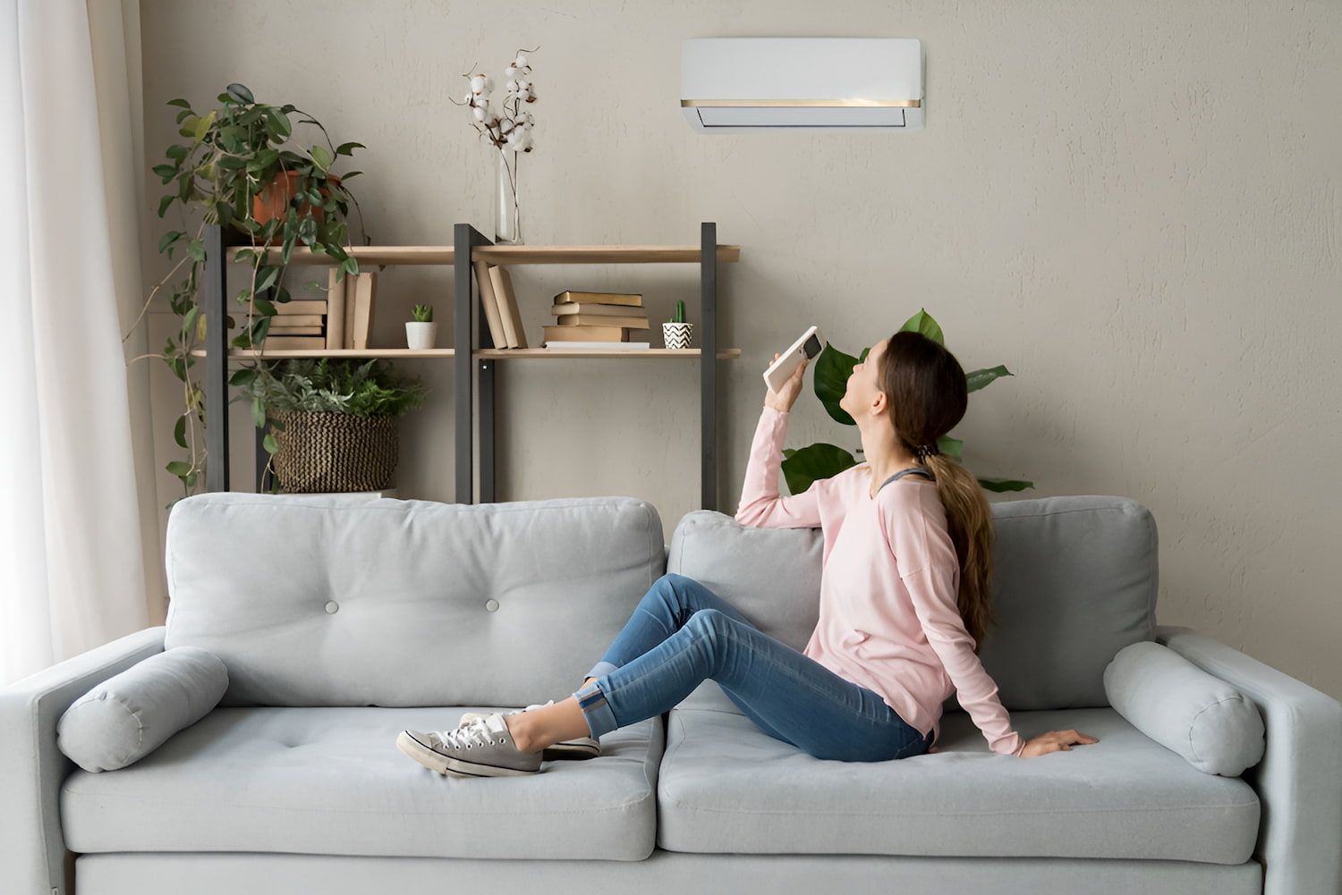 Woman on Sofa Adjusting Air Conditioner With Remote — Frosty Solutions Air Conditioning In Dunedoo, NSW