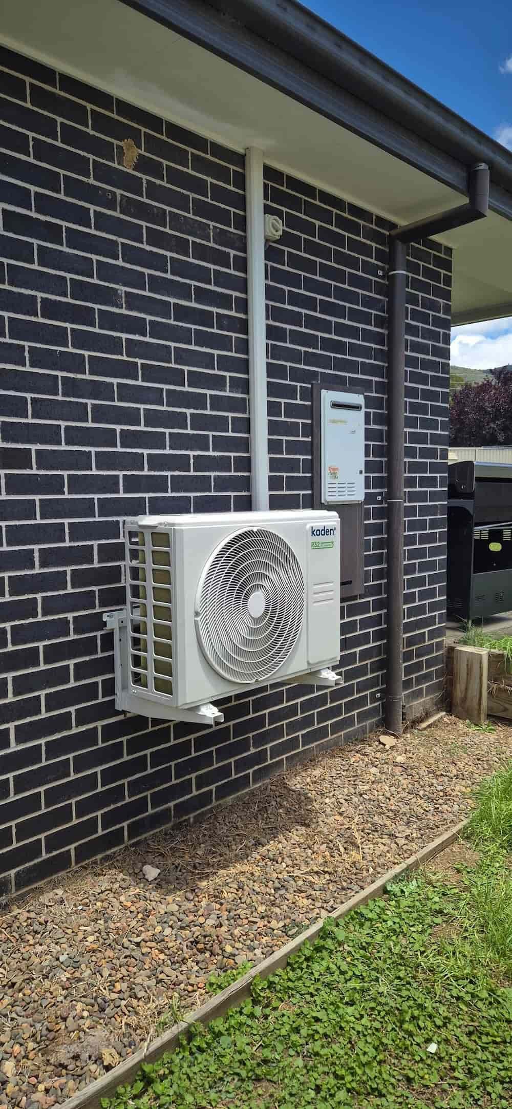Exterior Shot of a Dark Brick Wall With an Air Conditioning Unit — Frosty Solutions Air Conditioning In Lithgow, NSW