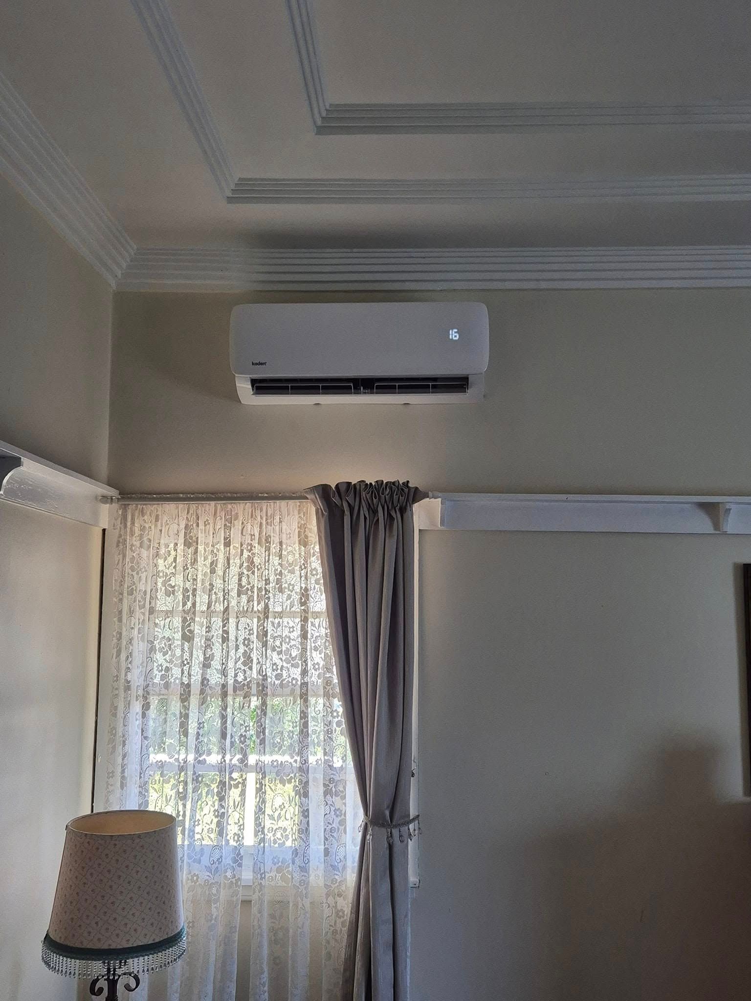 Air Conditioner Unit on a Wall Above a Window With Curtains and a Lamp — Frosty Solutions Air Conditioning In Mudgee, NSW