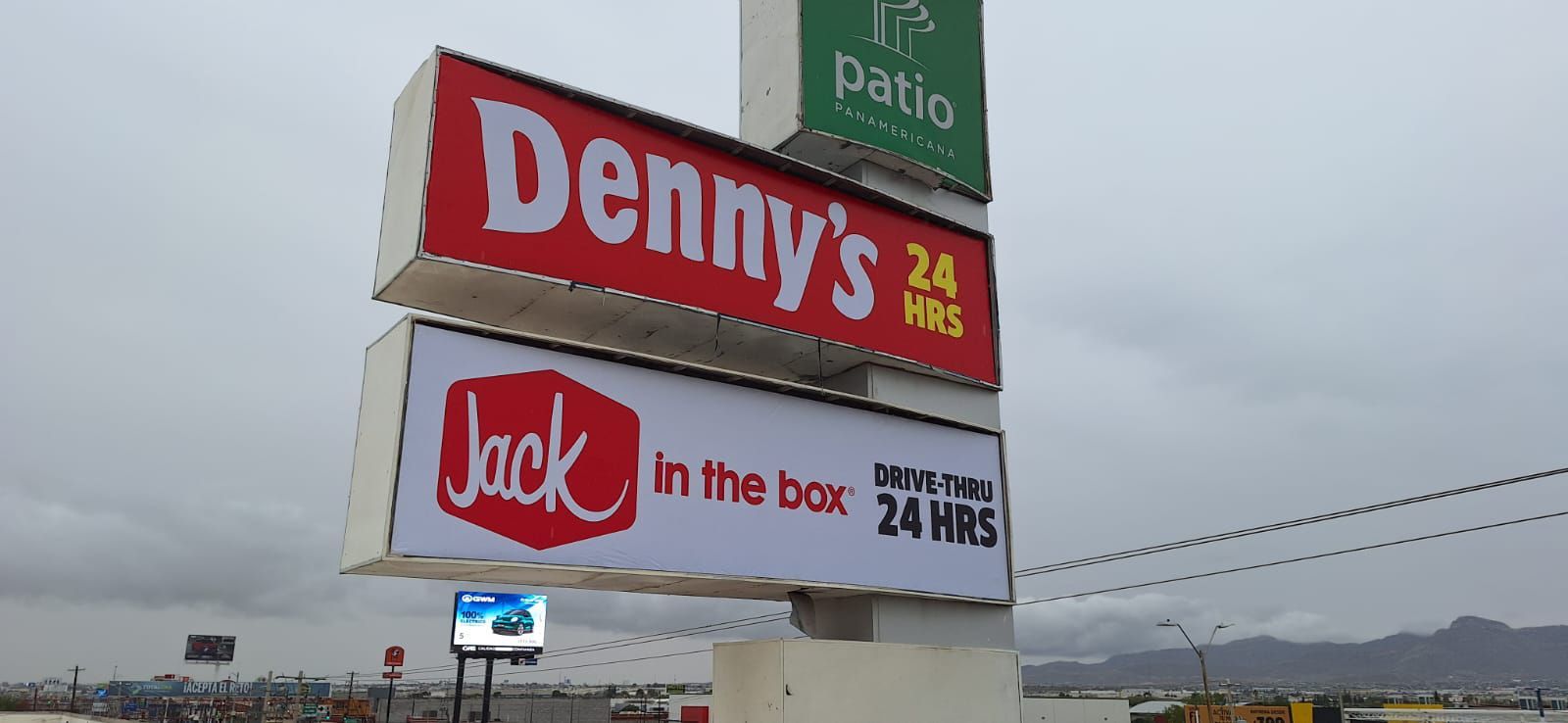 Letrero de un Denny's y un Jack in the Box, ambos abiertos las 24 horas. Cielo gris al fondo.