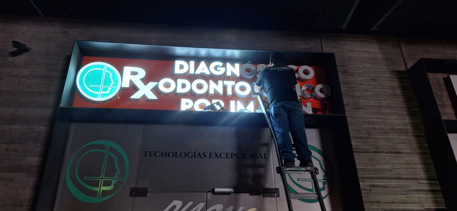 Una persona en una escalera trabajando en un cartel de una clínica que dice 