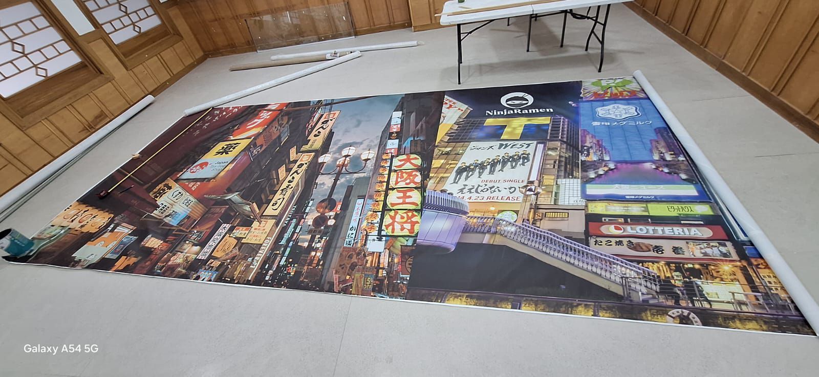 Gran cartel de una ciudad de noche con edificios muy iluminados, expuesto en el suelo.