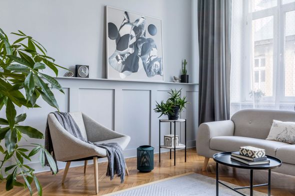 Bright living room with gray sofa, armchairs, plants, and abstract wall art by a window.