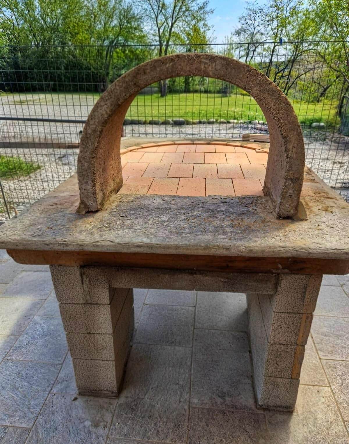 Un forno in mattoni è posizionato su un patio accanto a una recinzione.