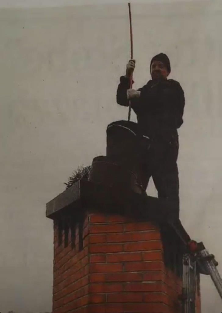 Spazzacamino è in piedi in cima a un camino di mattoni e tiene in mano uno strumento di pulizia