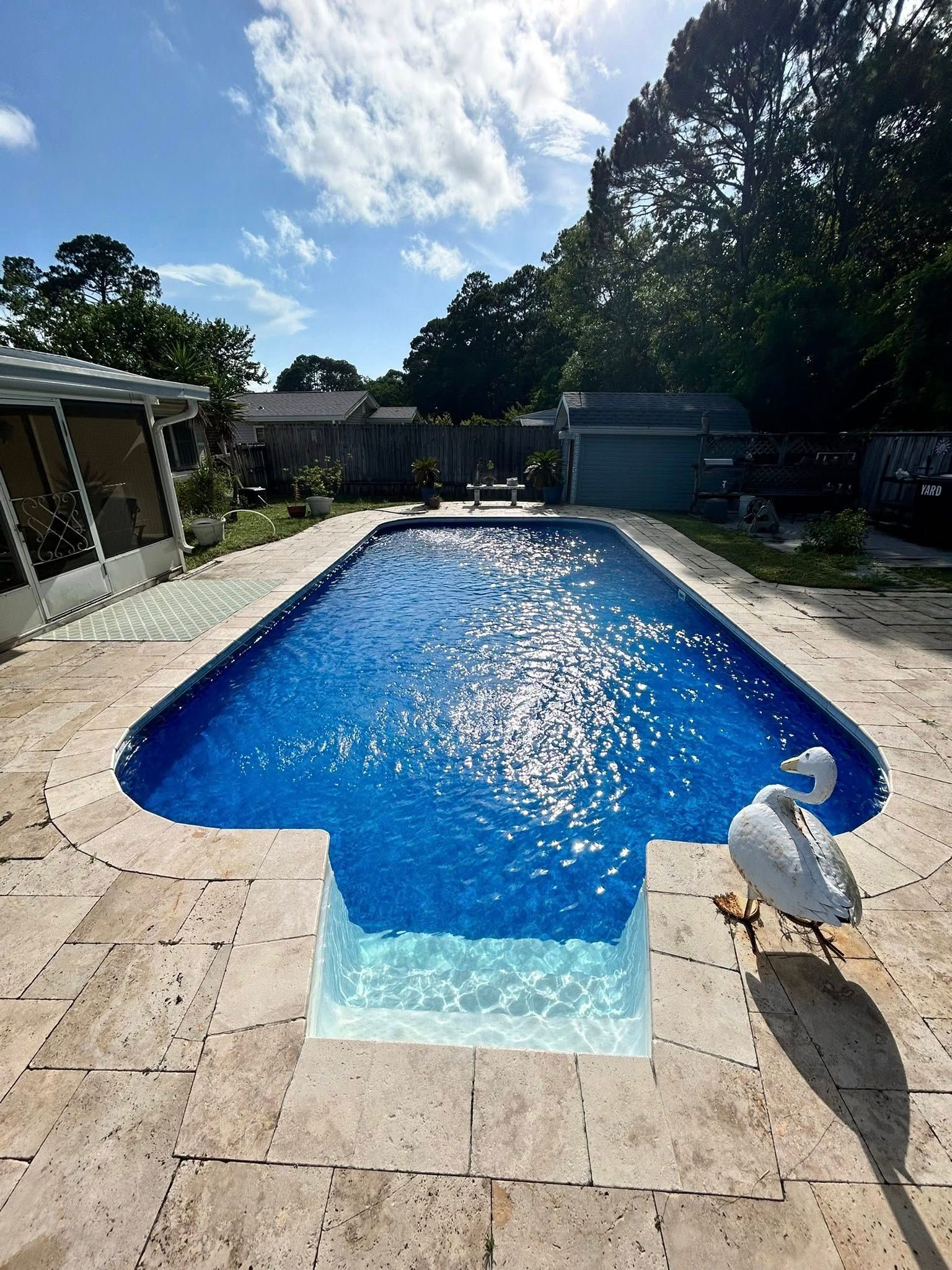 Pool with bright blue water, swan floaty, and tan tile patio under a sunny sky.