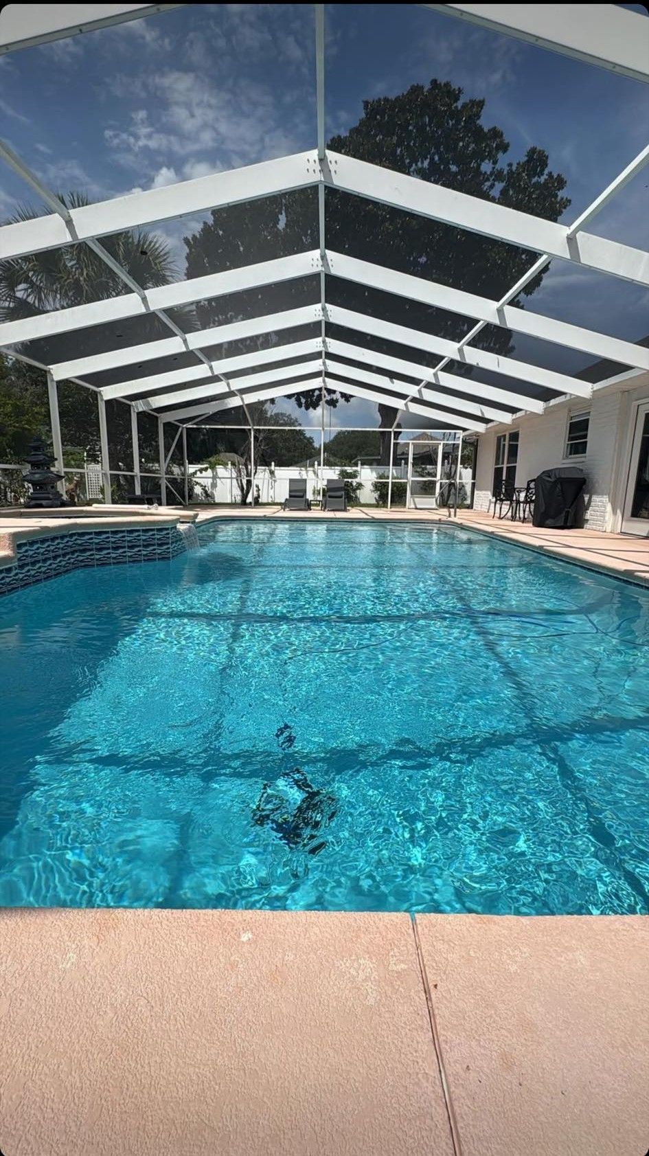 Pool enclosed by a screened roof, with clear blue water reflecting the sky and surrounded by a patio.