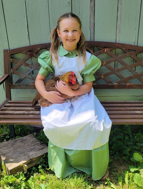 A little girl is sitting on a bench holding a chicken