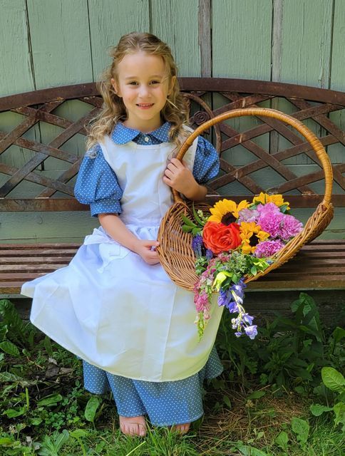 A little girl is sitting on a bench holding a basket of flowers.